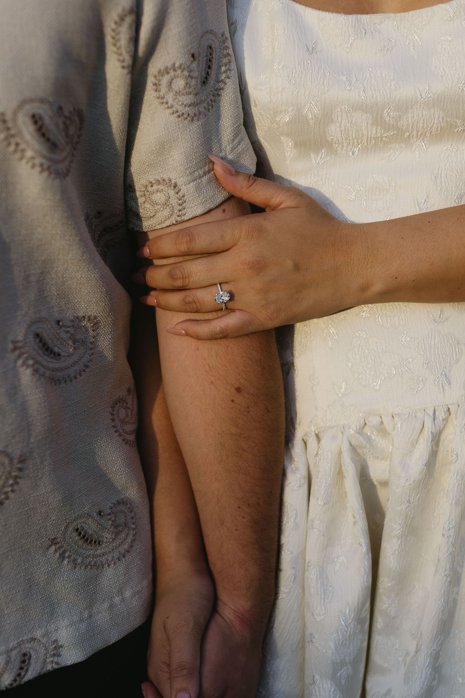 Close-up shots of hands against white fabric showing engagement ring details.
