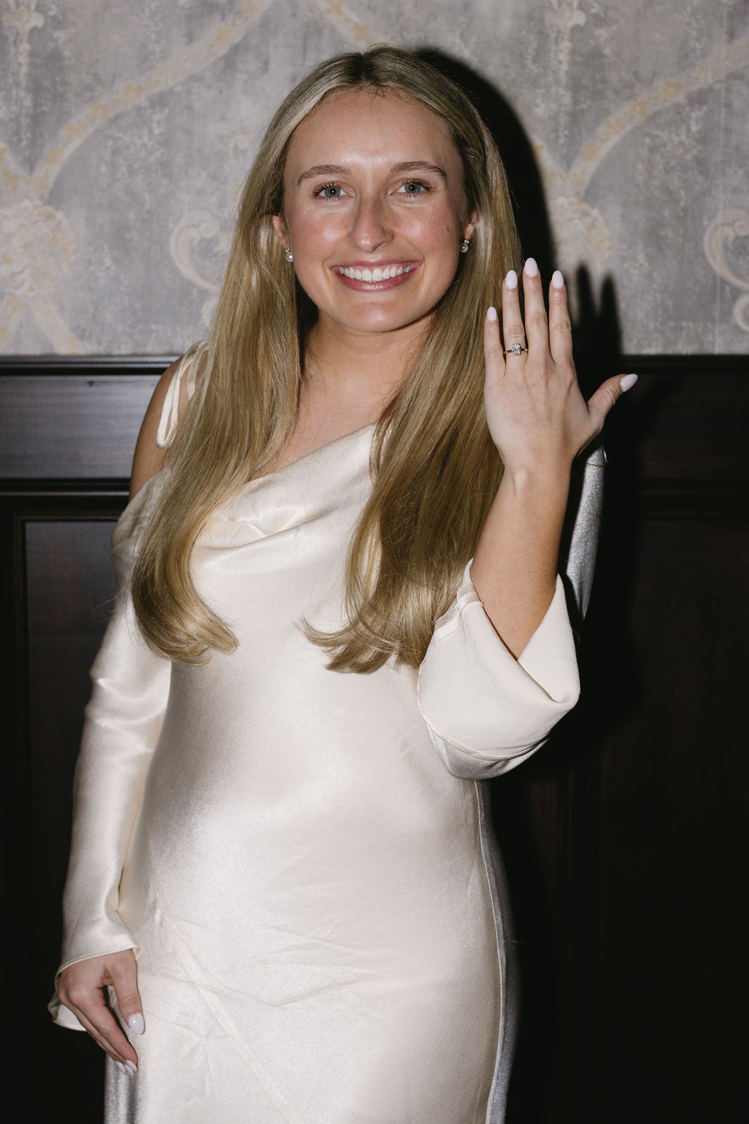 Person in white dress smiling and posing against grey wall at an event.