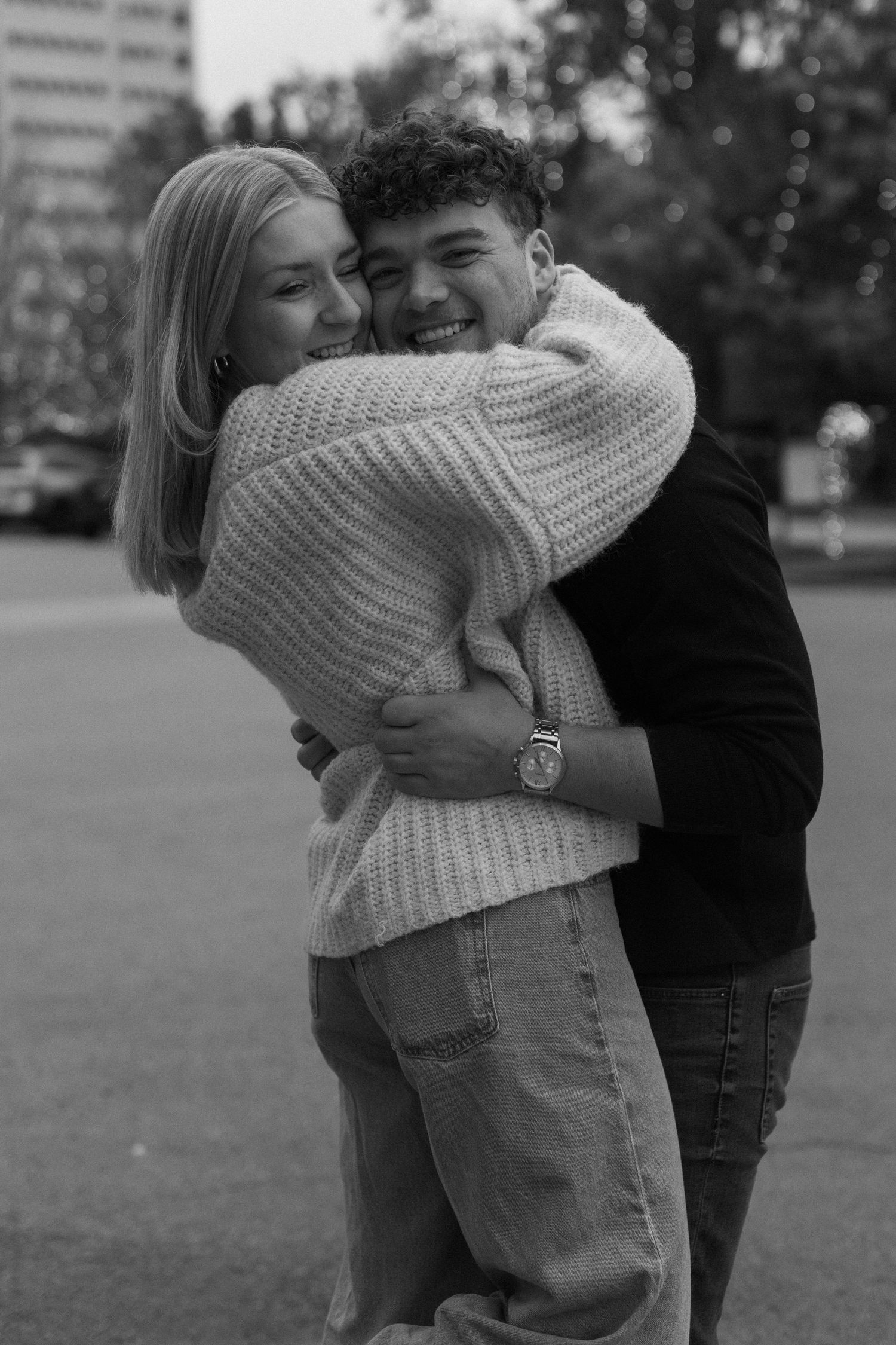 A black and white portrait of a couple sharing a warm embrace in an urban setting.