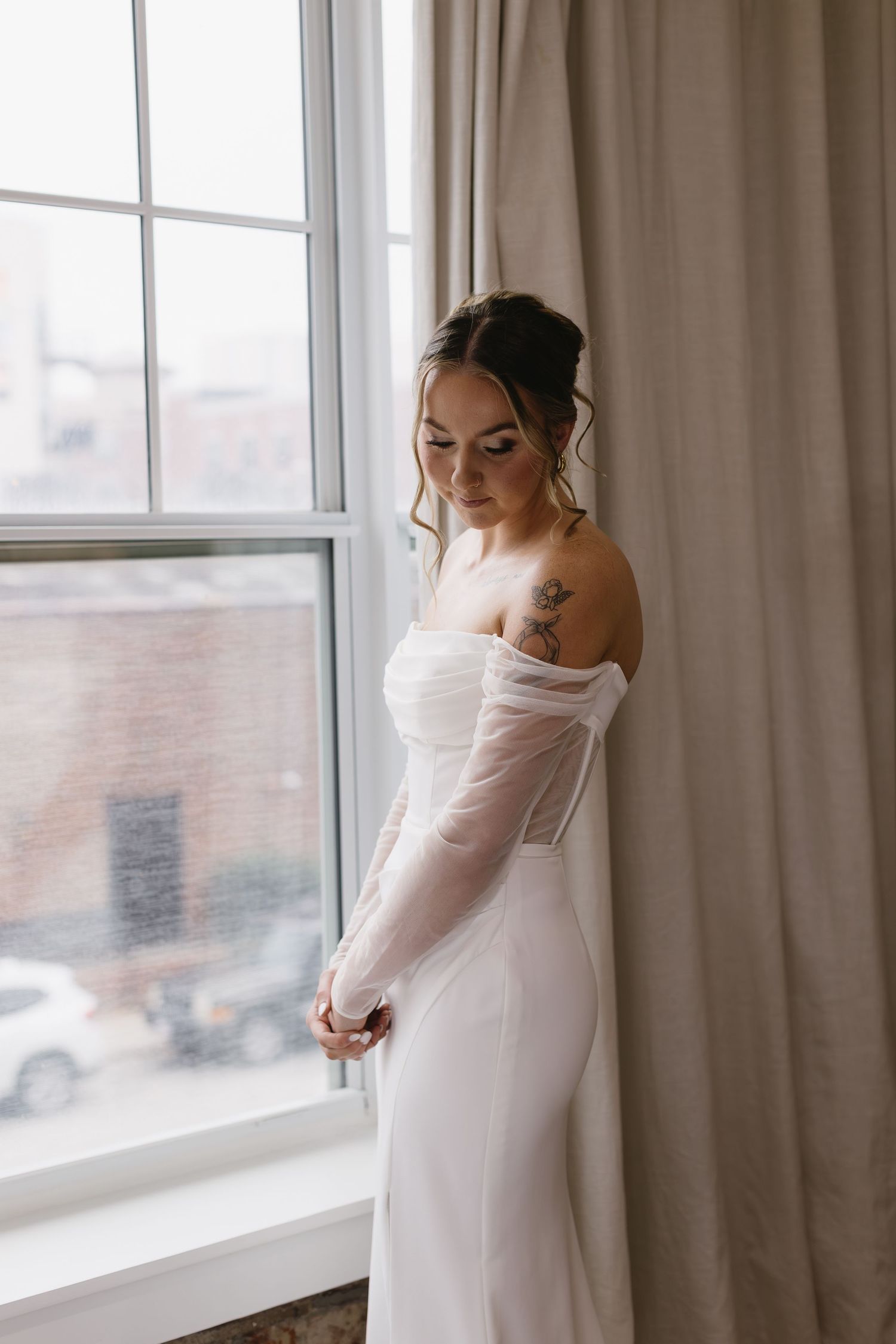 Elegant white wedding dress with sheer long sleeves photographed near a bright window.