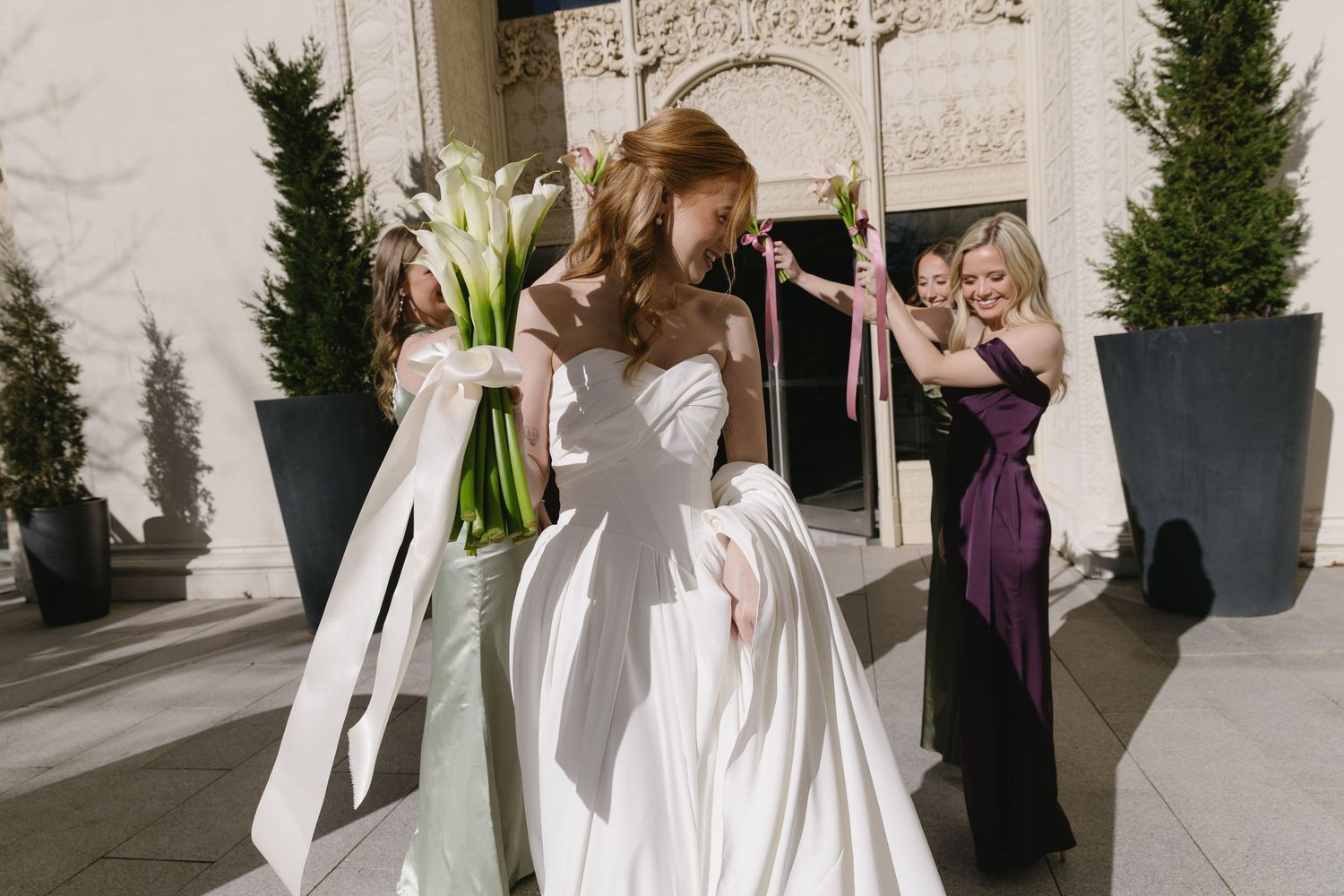 Wedding party members in purple and white attire gathered outside contemporary building entrance.