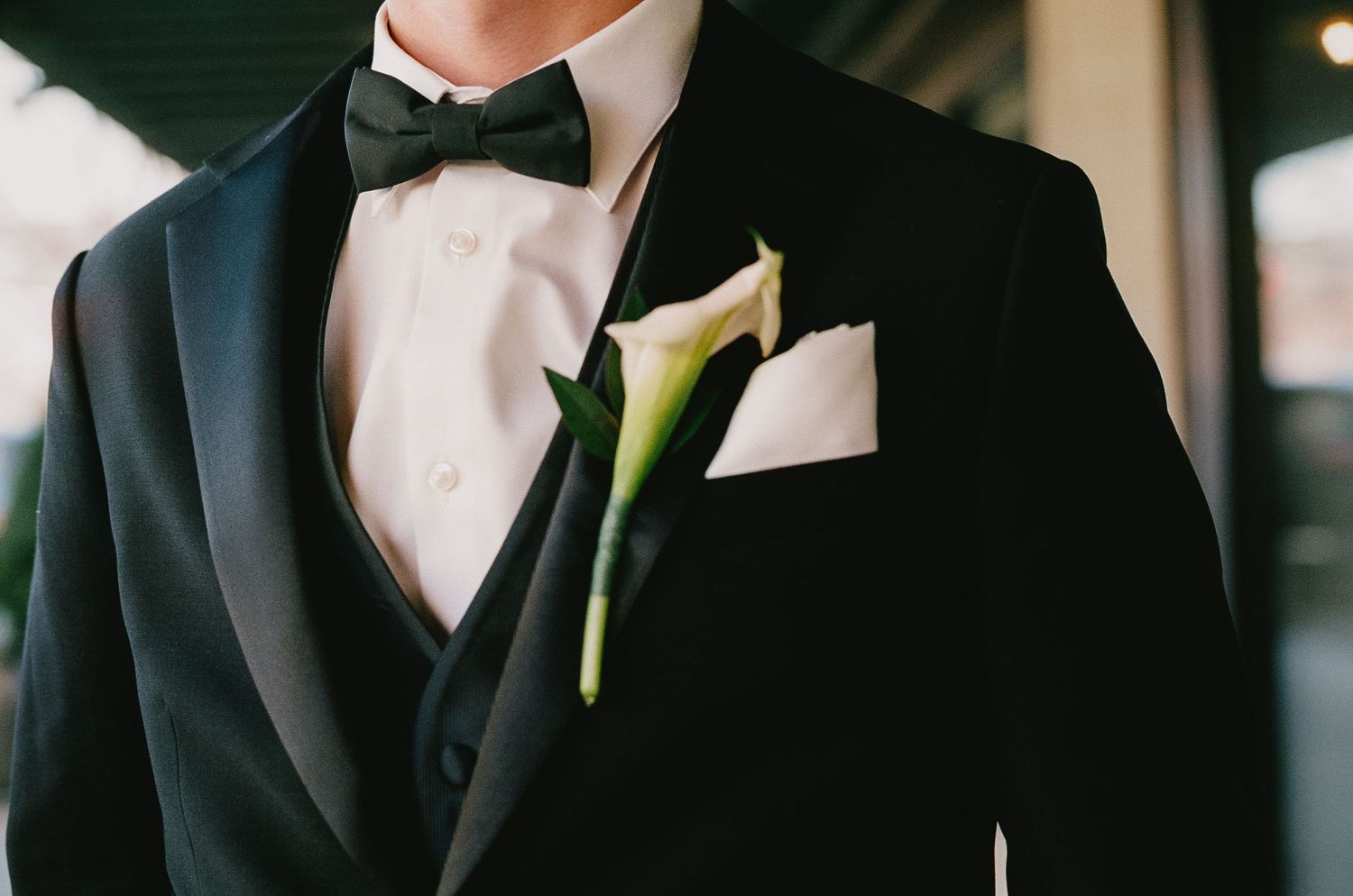 Close-up details of groom's formal black tuxedo with white boutonniere.