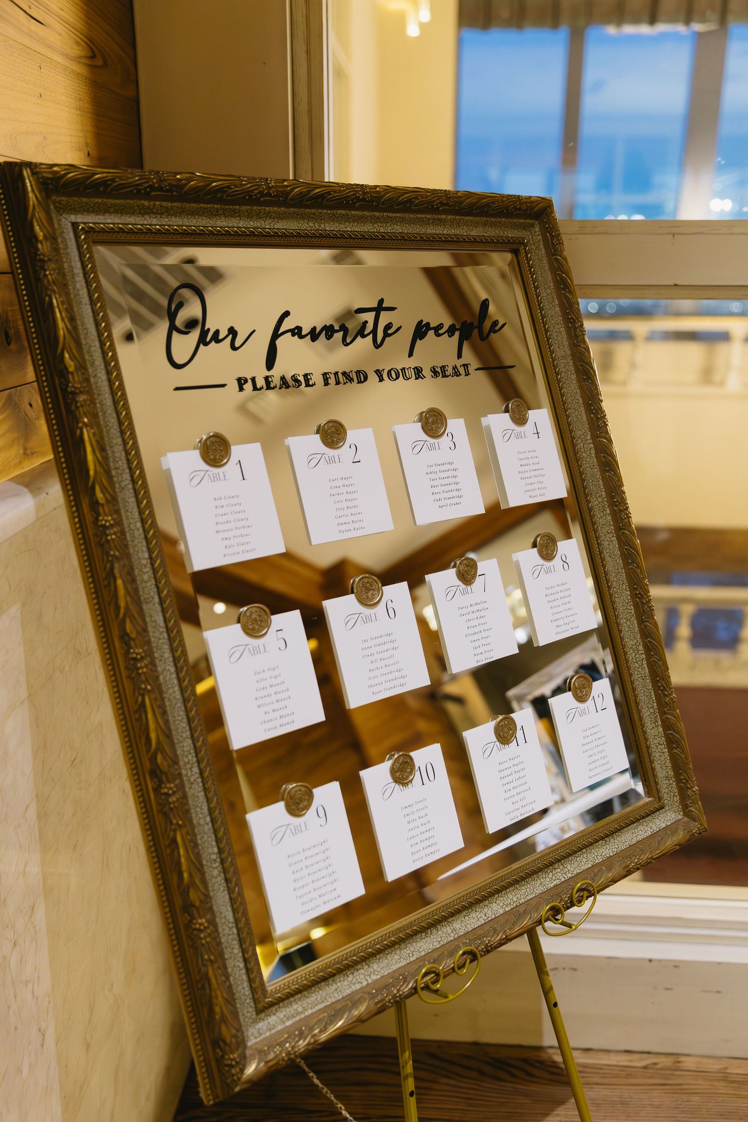 Elegant gold-framed seating chart display with paper cards for wedding guest table assignments.