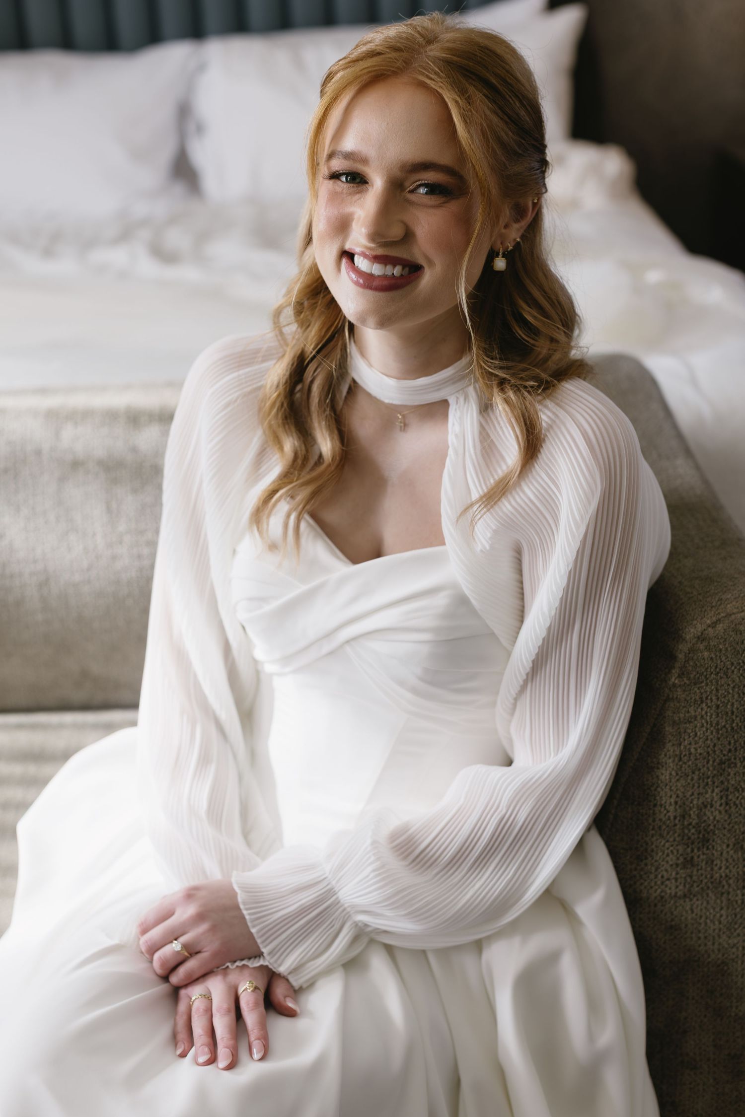 Portrait of a radiant bride wearing a white long-sleeved gown with soft wavy hair styling.