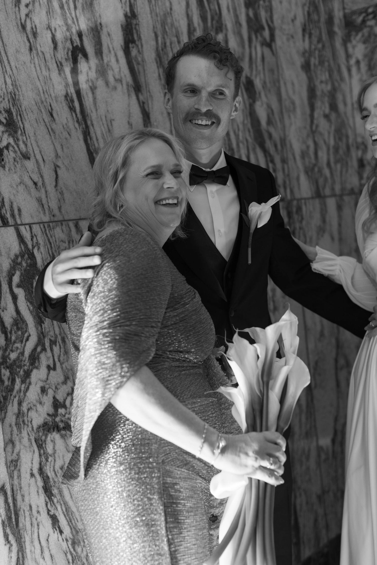 Wedding party members share laughter against a textured marble wall background.