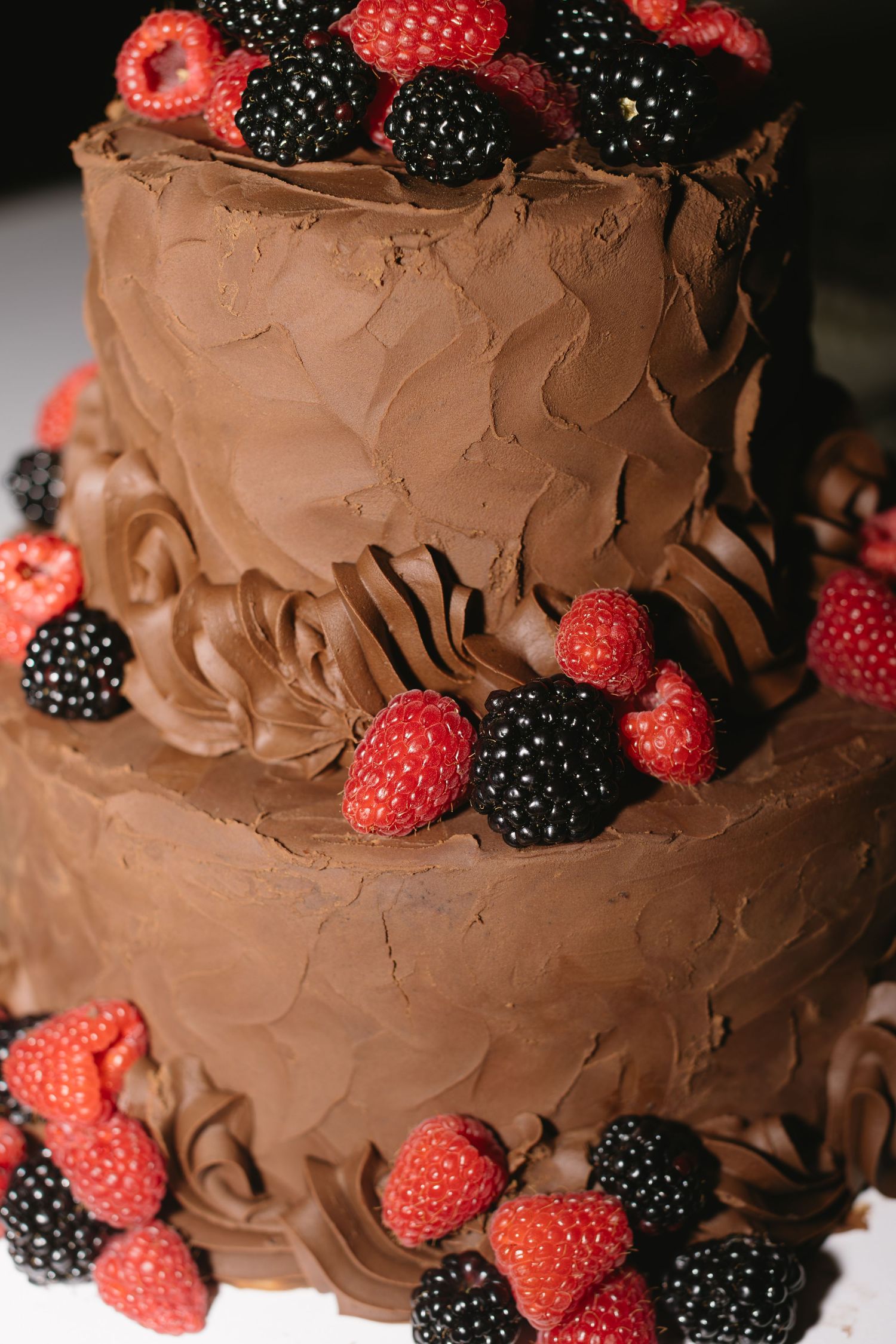 Two-tiered chocolate cake decorated with fresh raspberries and blackberries.