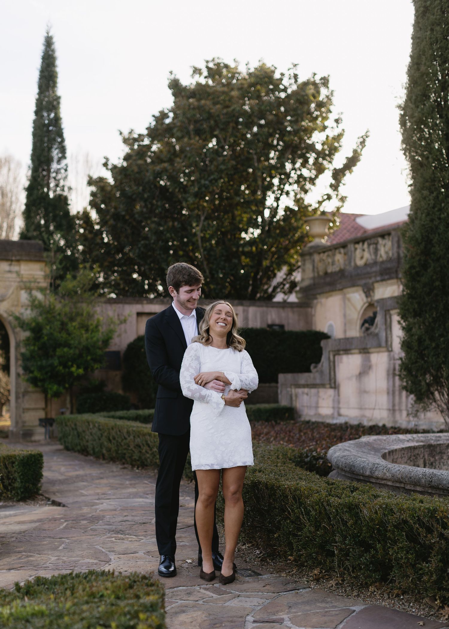A romantic wedding photoshoot sequence in a garden setting with cypress trees and stone architecture.