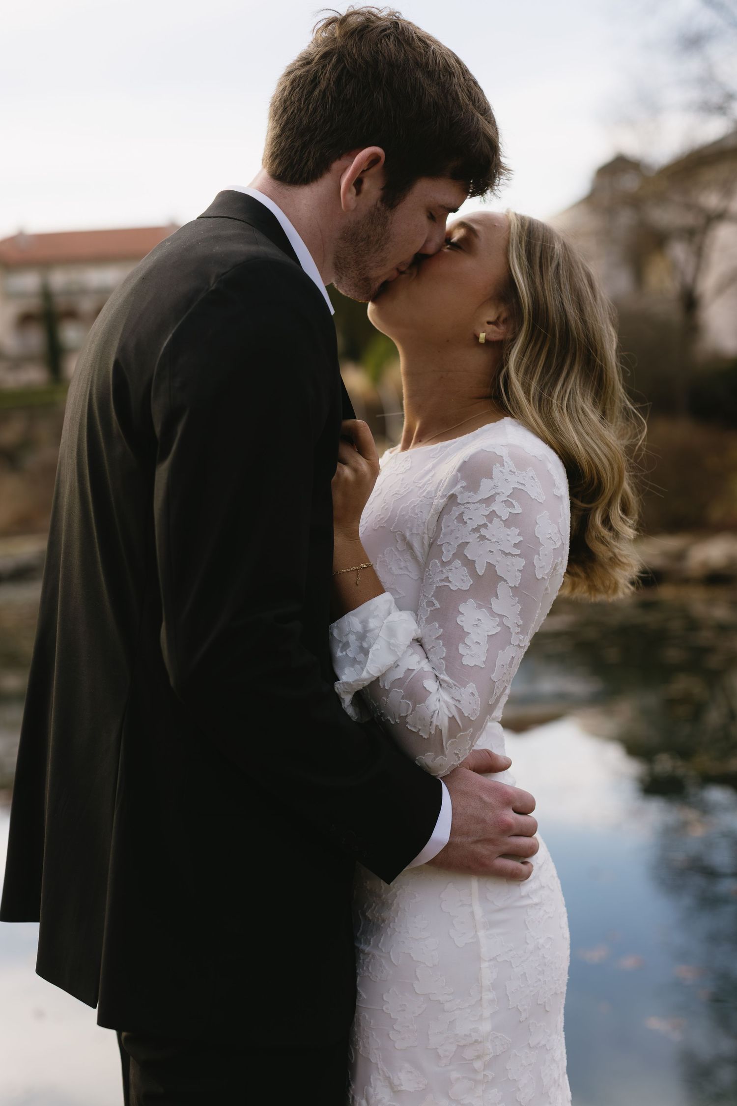 A romantic kiss shared between a couple in formal wear beside a reflective pool.