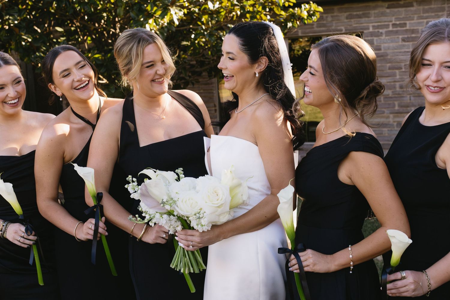 A joyful wedding party laughs together during outdoor group photos.