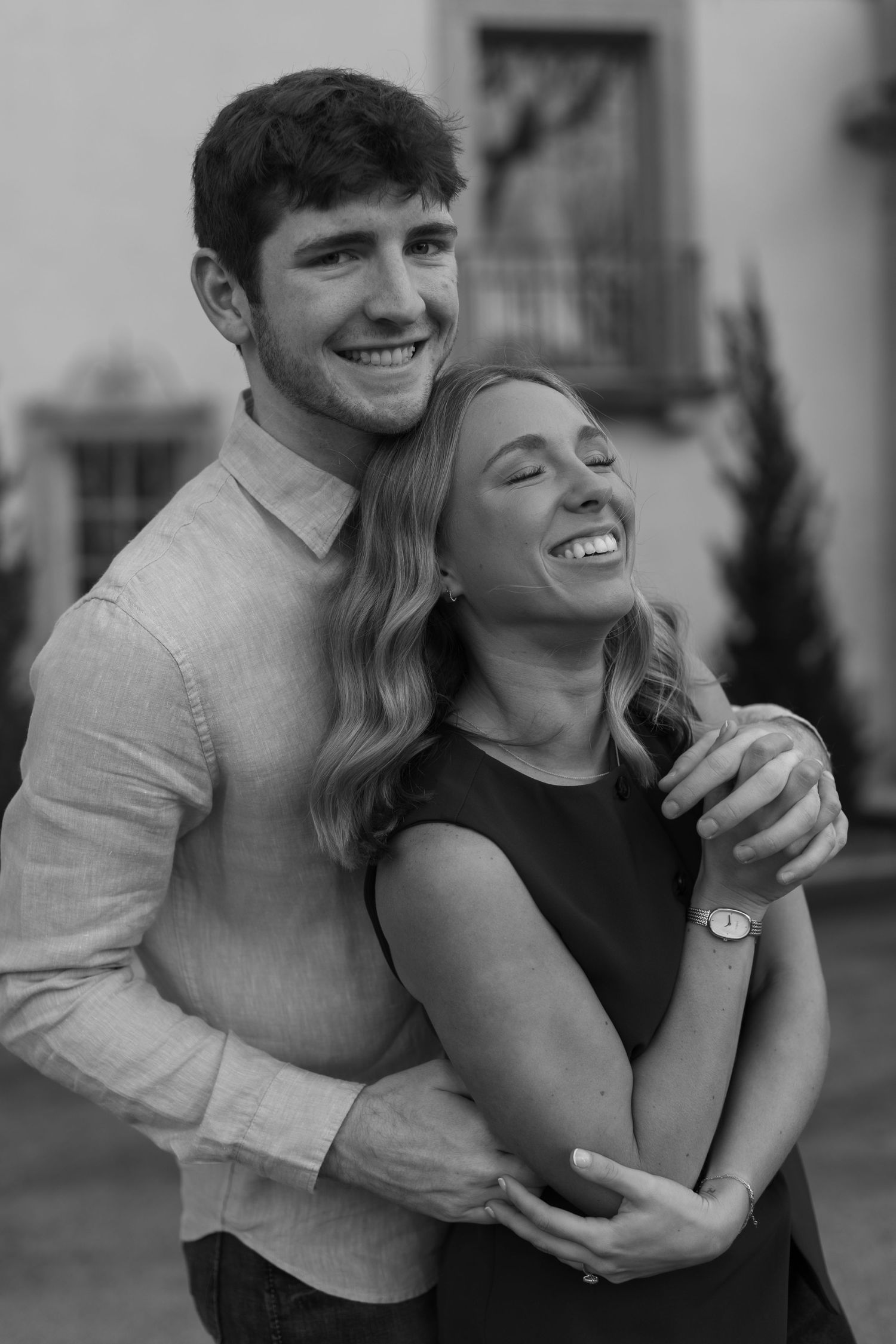 Playful black and white portrait of a couple laughing and embracing outdoors.