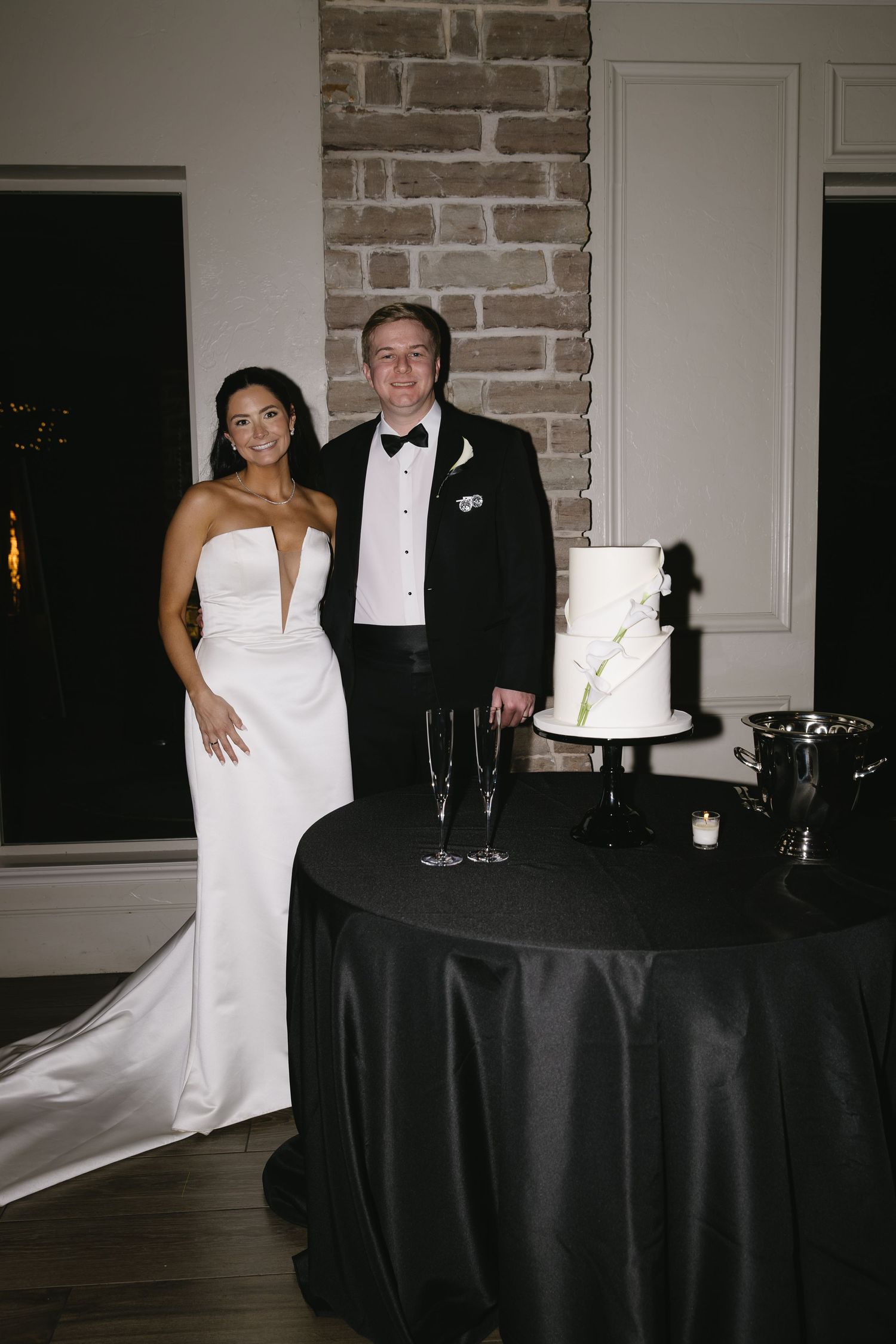 Elegant wedding reception setup with white cake and brick accent wall.