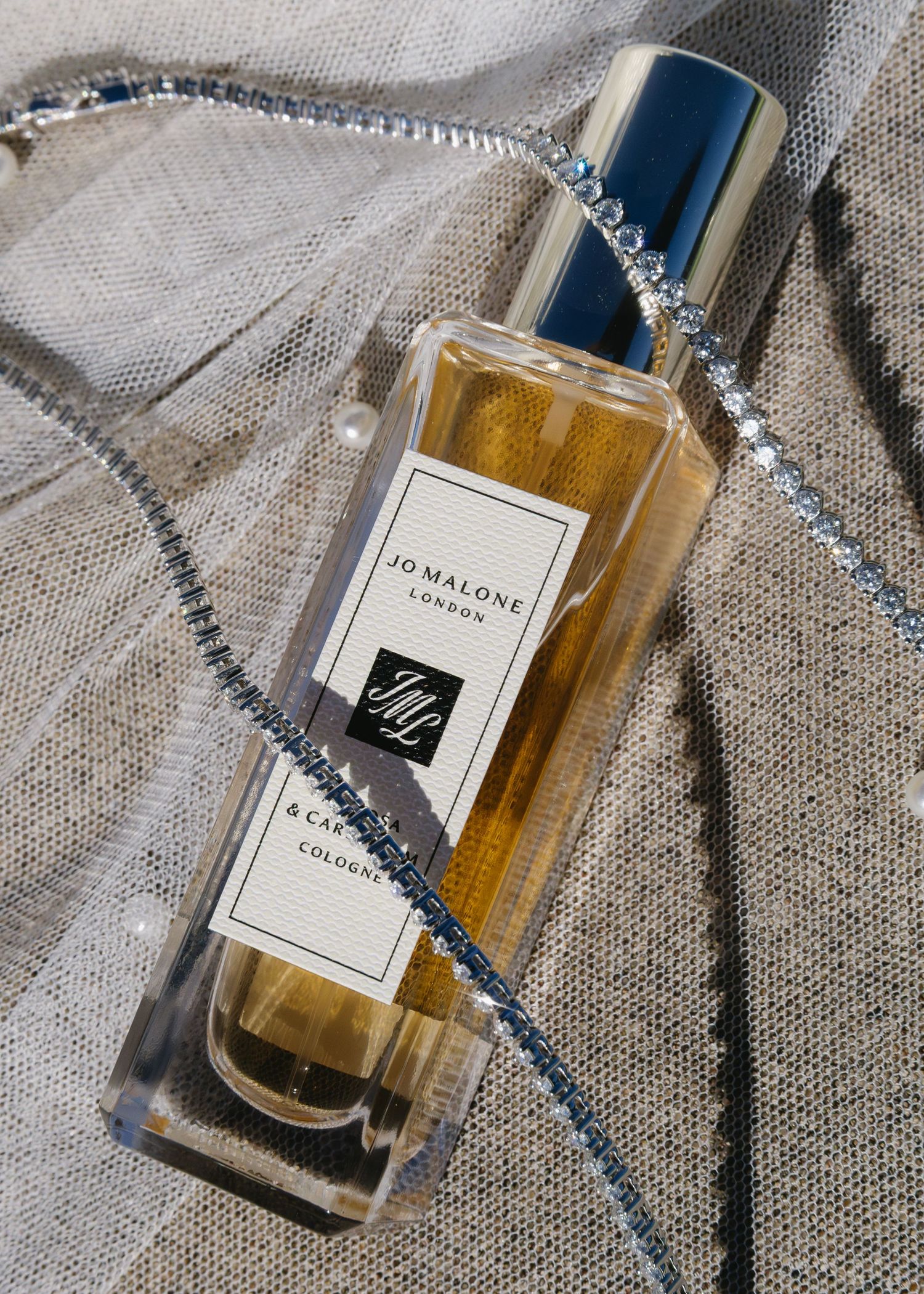 Jo Malone perfume bottle with silver chain photographed on neutral background.