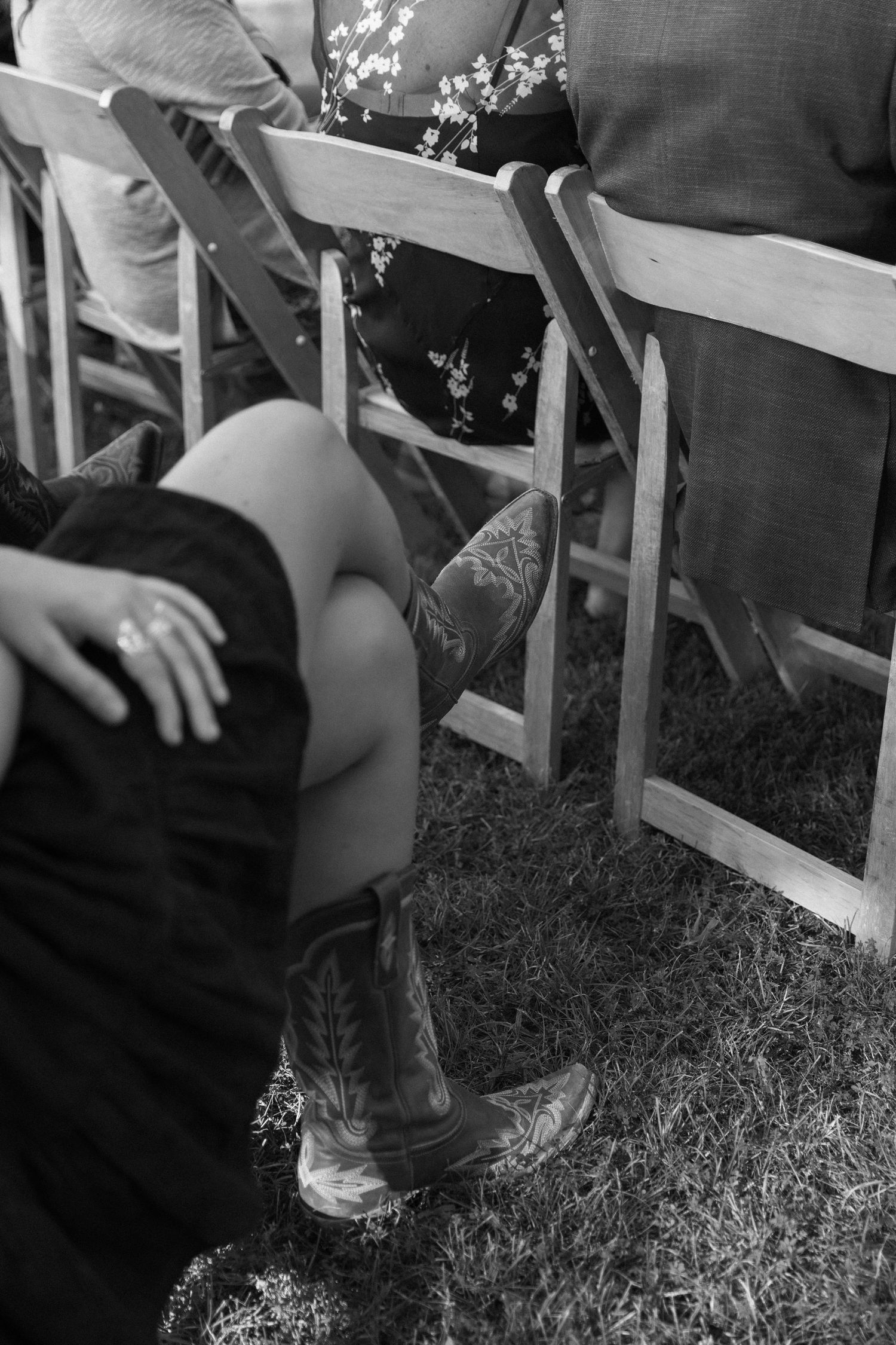 Low angle black and white shot of guests' legs at an outdoor wedding ceremony.