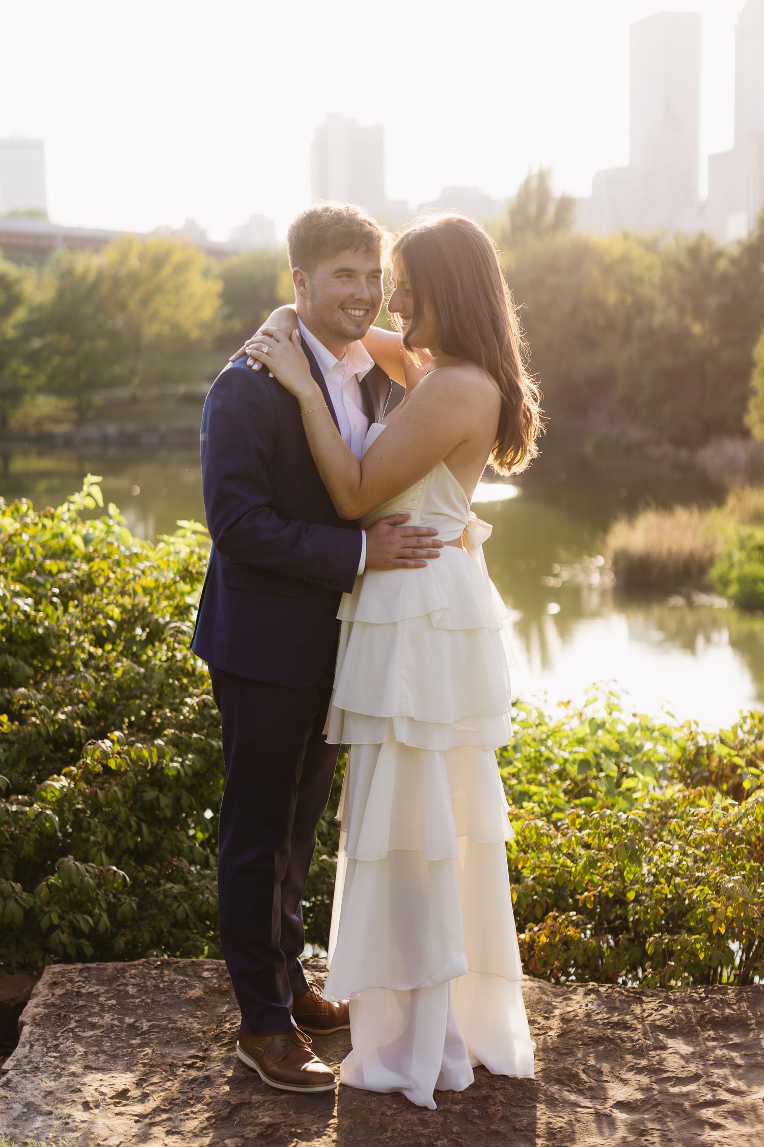 A tender embrace photographed during golden hour with water and greenery in the background.