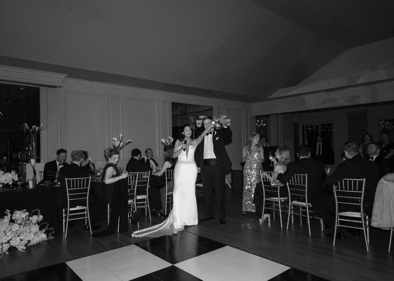 Black and white panoramic view of an empty ballroom with elegant chairs and tables arranged for an event.