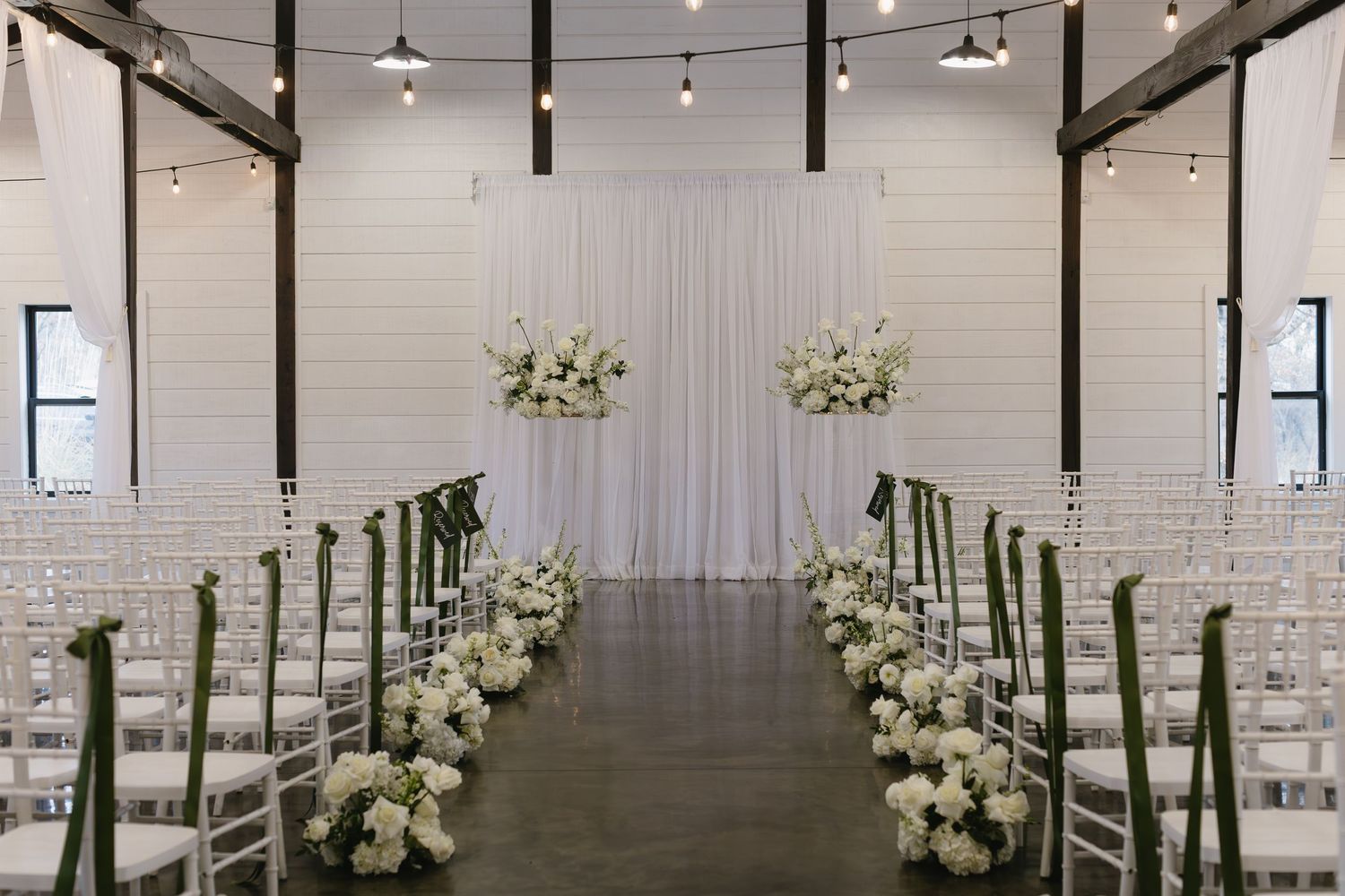 Modern minimalist wedding ceremony space with white floral arrangements and industrial ceiling.
