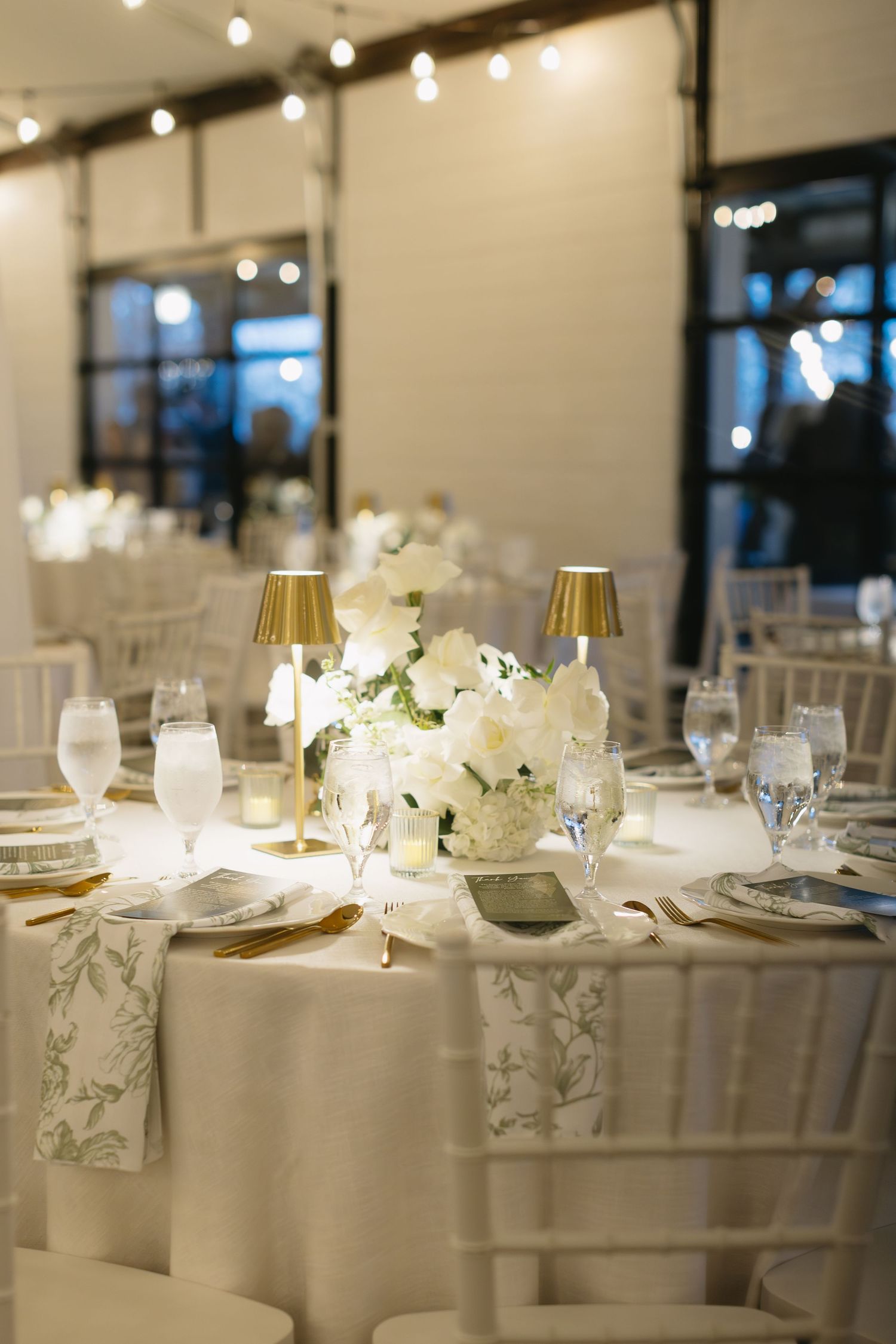 Beautifully decorated wedding reception tables with white linens and floral arrangements under warm lighting.