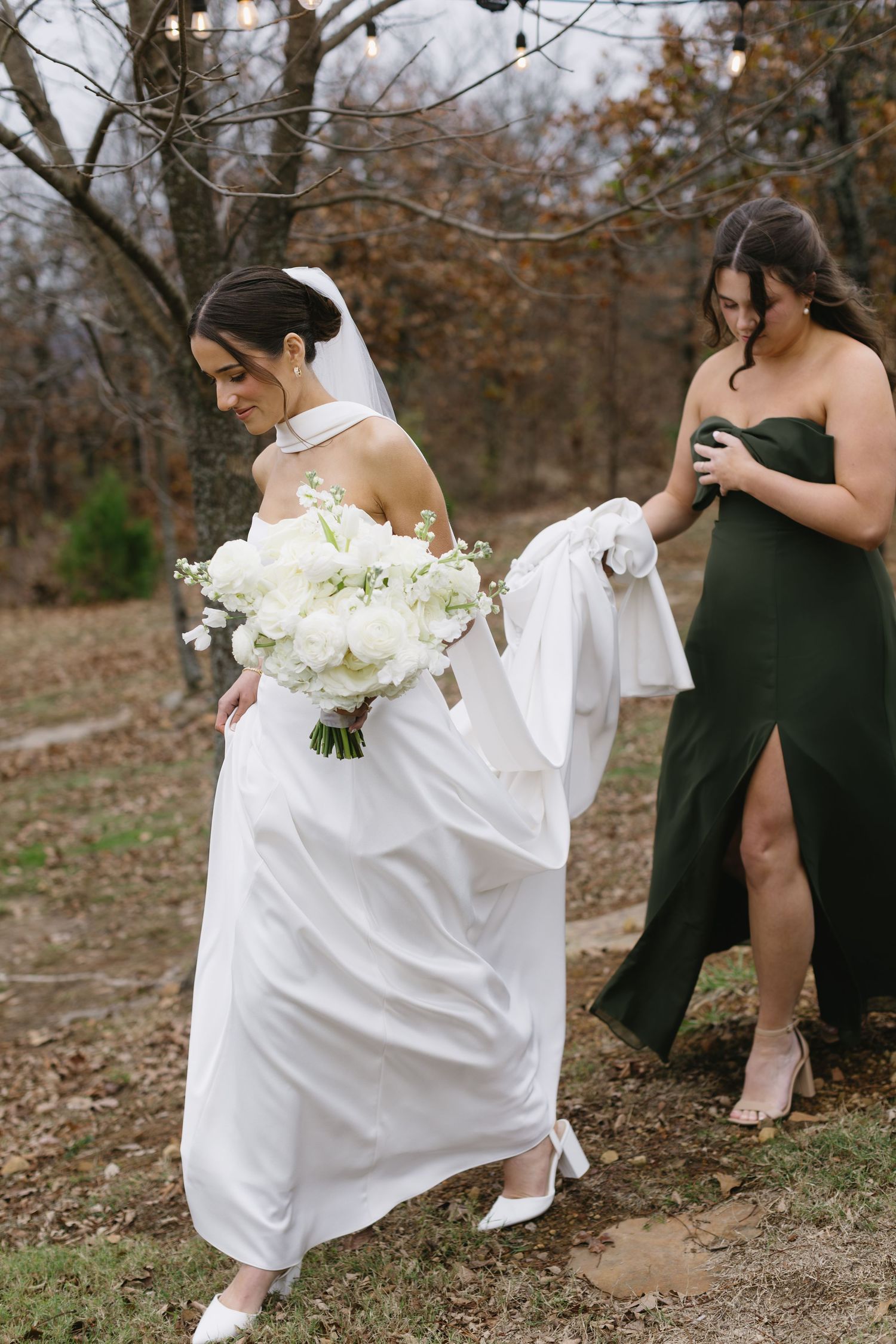 Wedding party members in black dresses gather outdoors among autumn leaves.