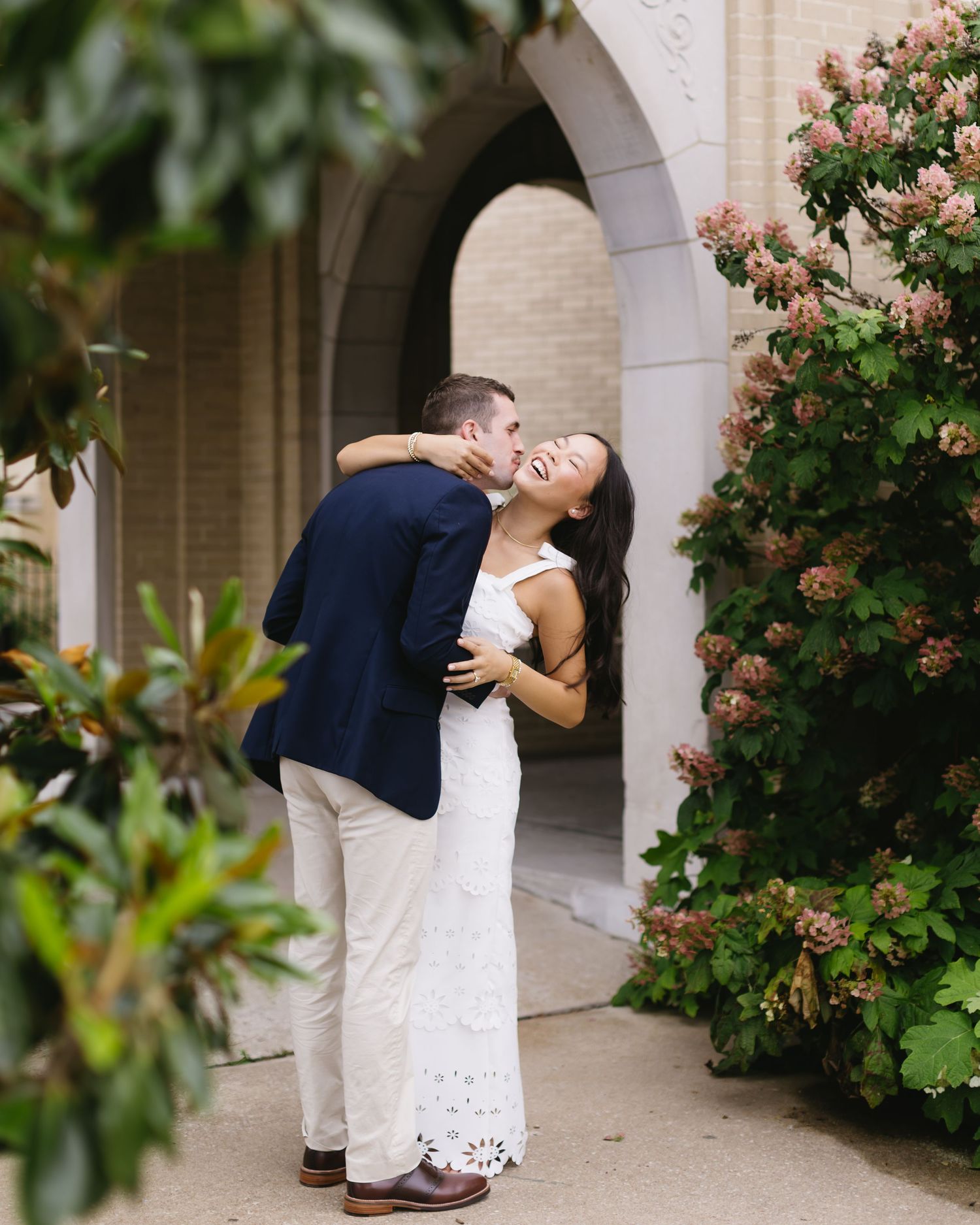 Romantic couple shares intimate moment under arched walkway surrounded by blooming flowers.