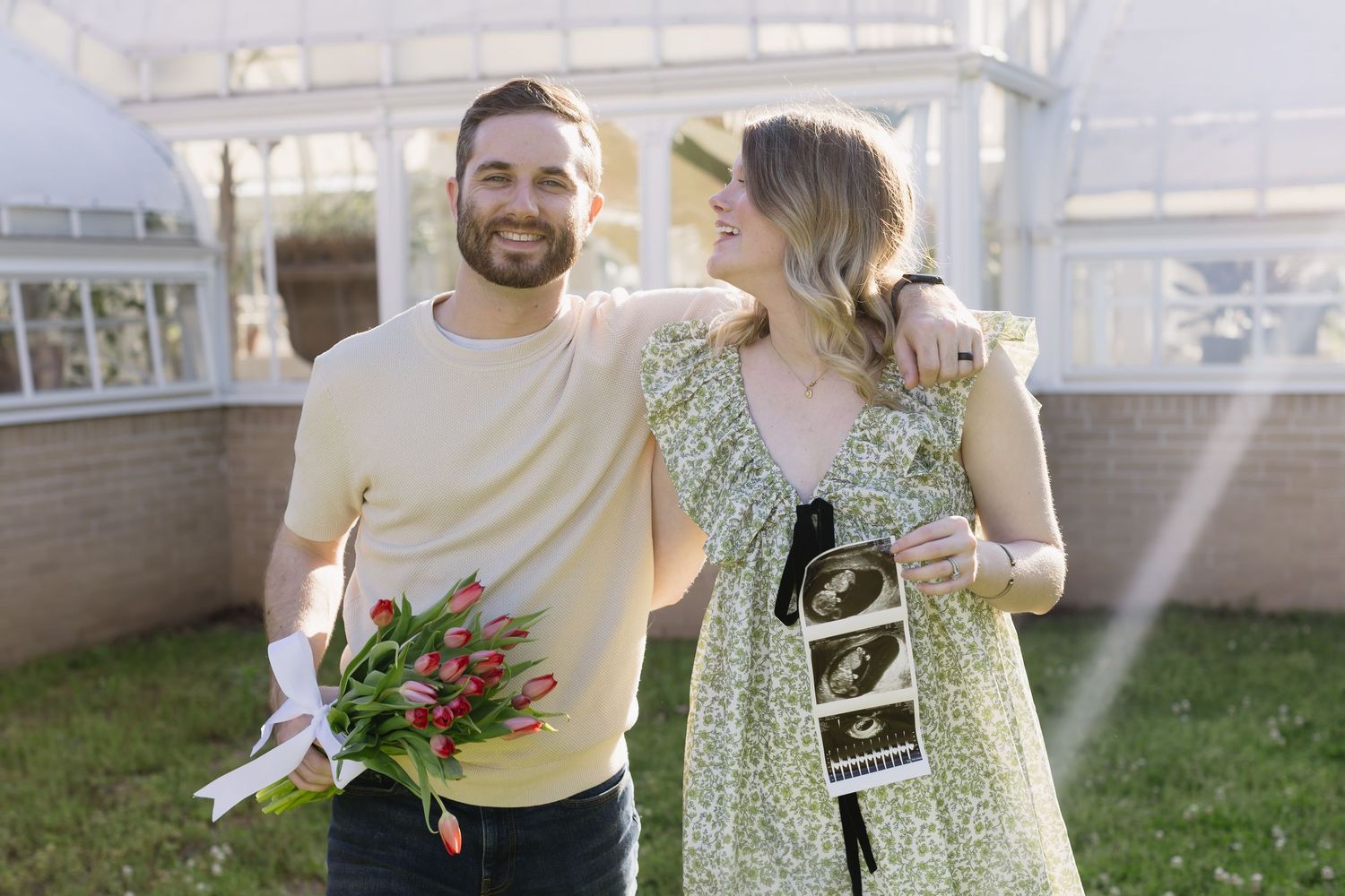 Couple sitting and laughing on steps while drinking beverages and holding fresh flowers and coffee cups.