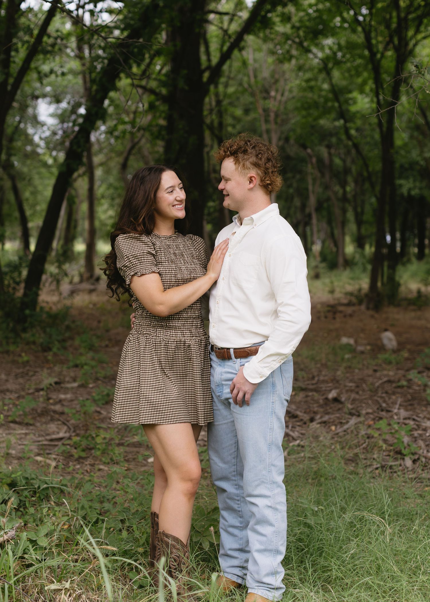 A couple shares intimate moments in casual summer outfits against a wooded natural backdrop.