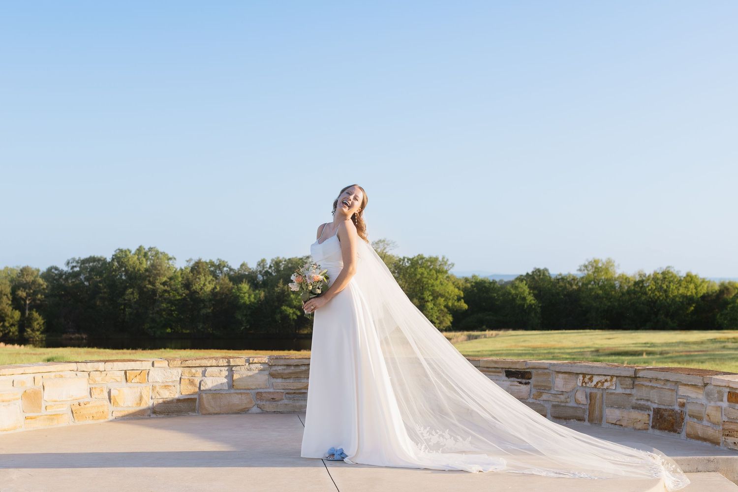 Romantic bridal portraits on a stone patio showcasing the dress train and veil in natural light.