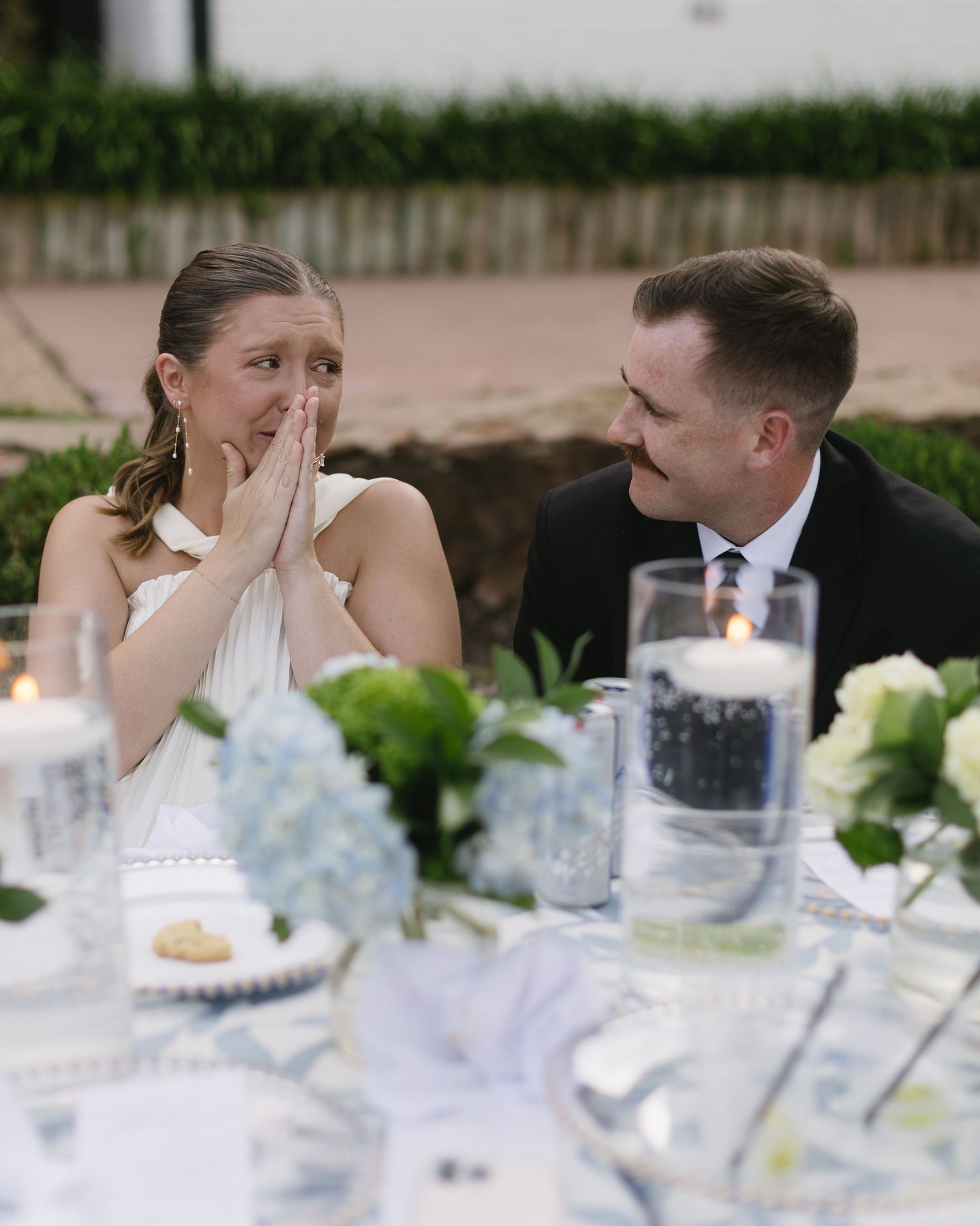Elegant wedding reception table setting with white flowers and romantic couple in background.