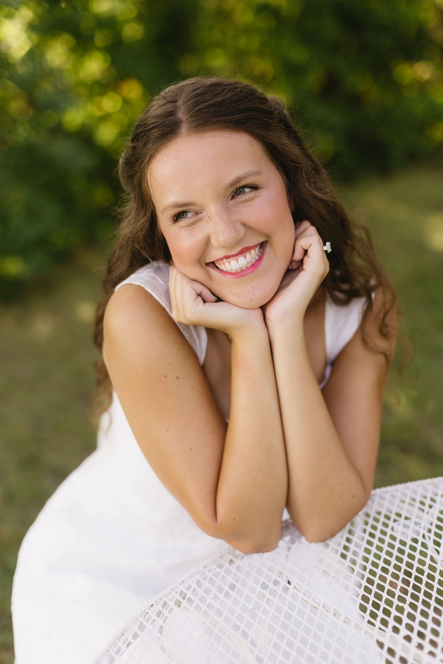 A radiant bride poses at a white garden table with natural greenery in background.