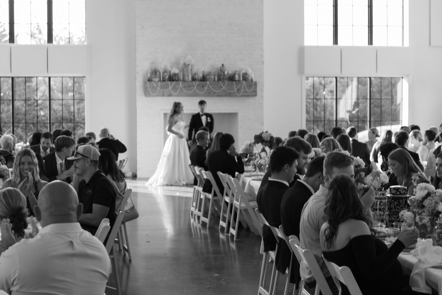 Black and white photo of wedding ceremony venue with guests seated in bright interior space.