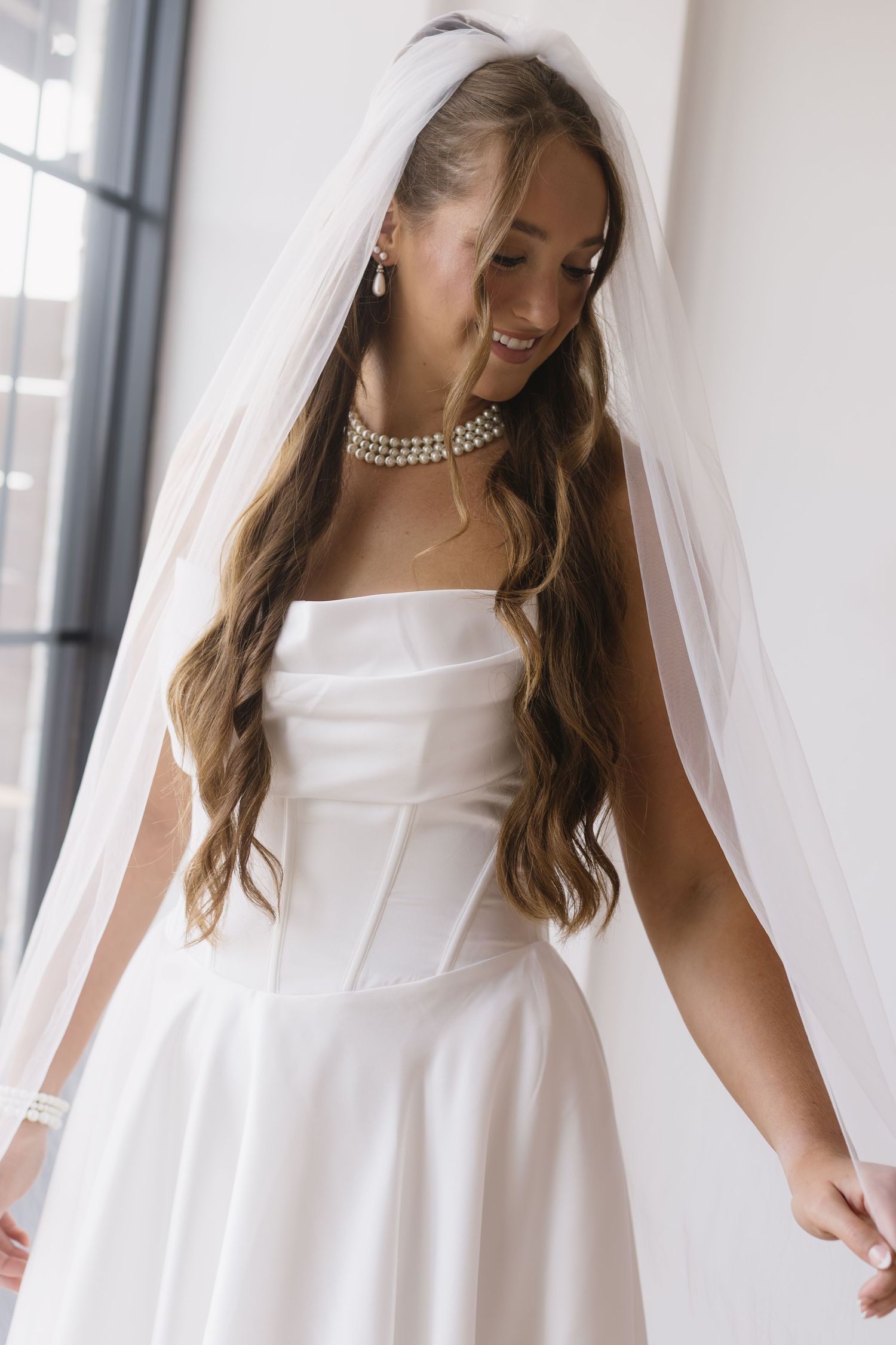 A bride in an elegant white wedding dress showing details of pearl neckline and flowing veil.