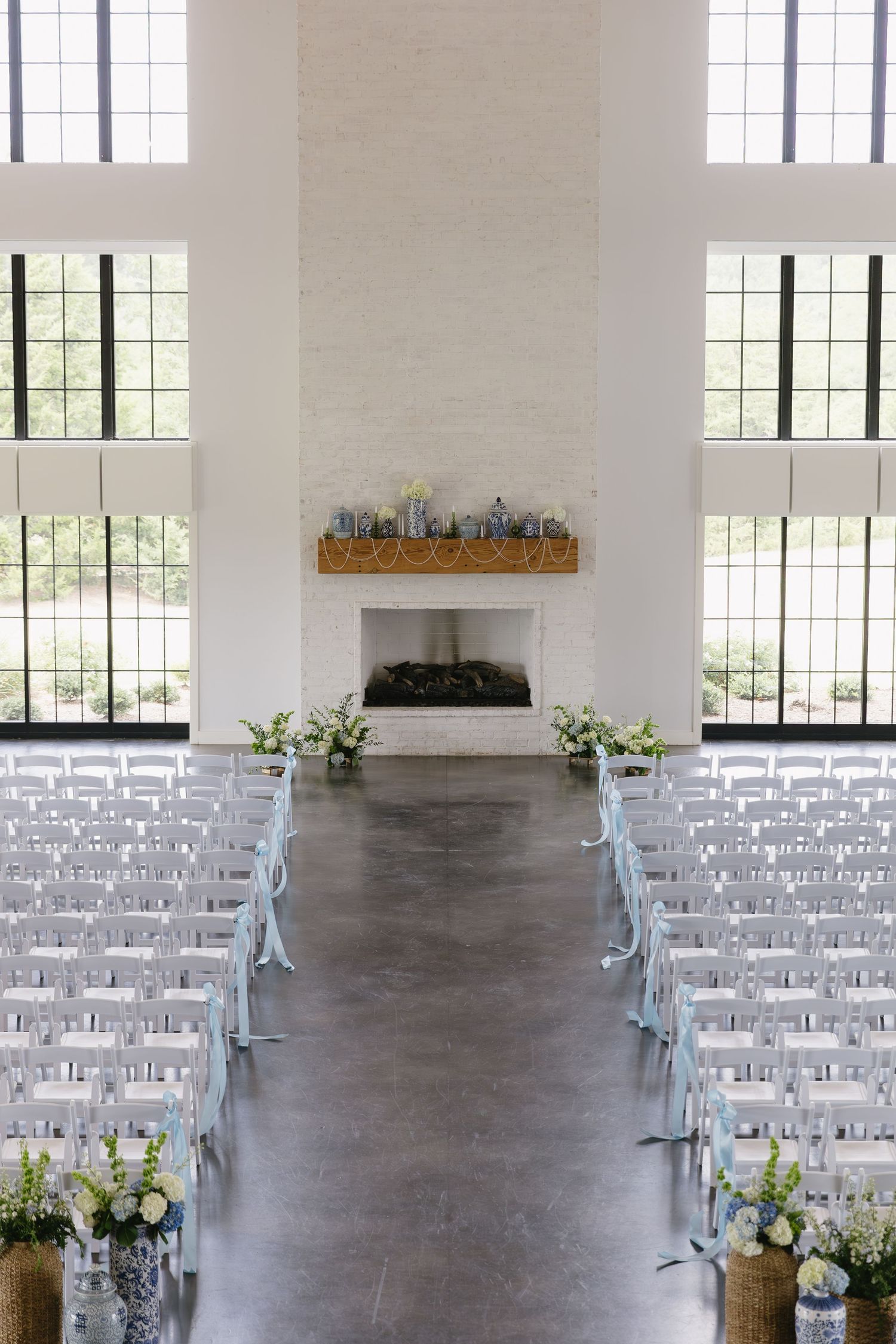 Modern wedding ceremony setup with white chairs and floral decorations in an industrial-style venue.