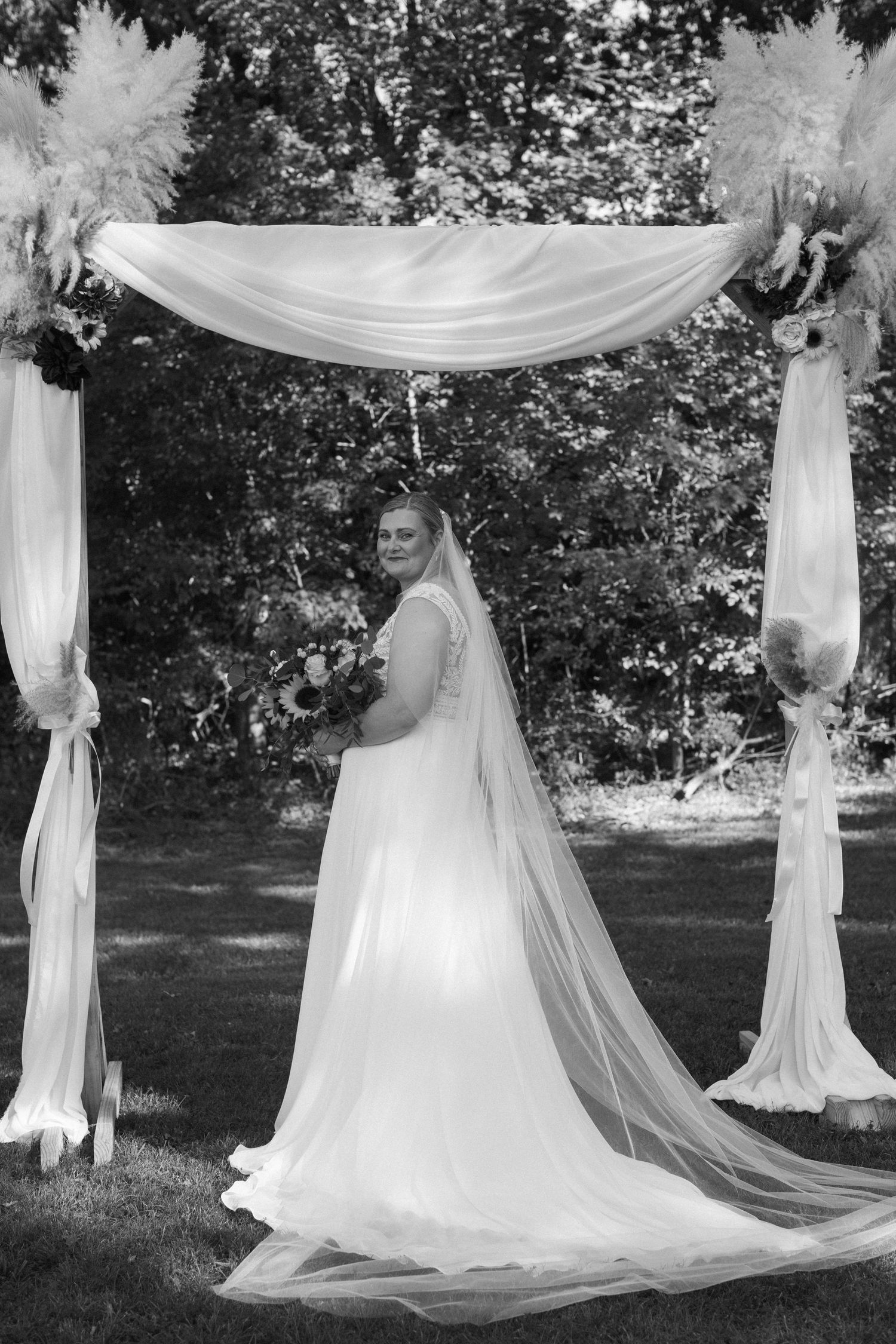 A wedding ceremony arch with flowing white fabric draped between posts in an outdoor garden setting.