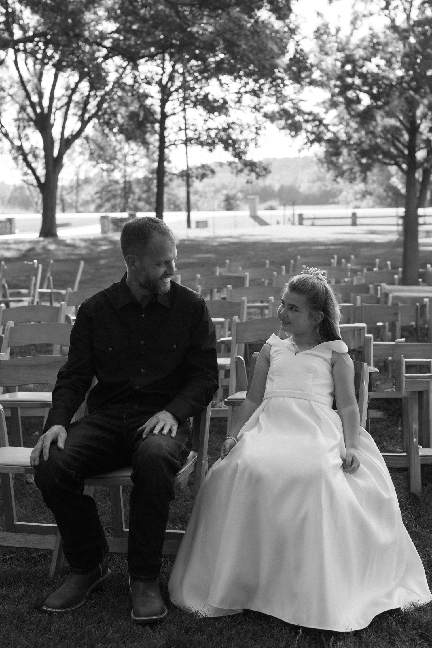 Wedding couple sitting together on wooden chairs in an outdoor setting.