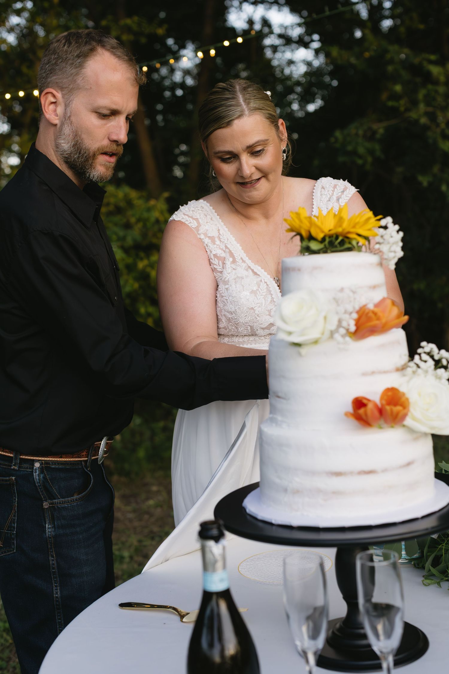 A couple cuts into their elegant white wedding cake adorned with fresh flowers and decorative details.