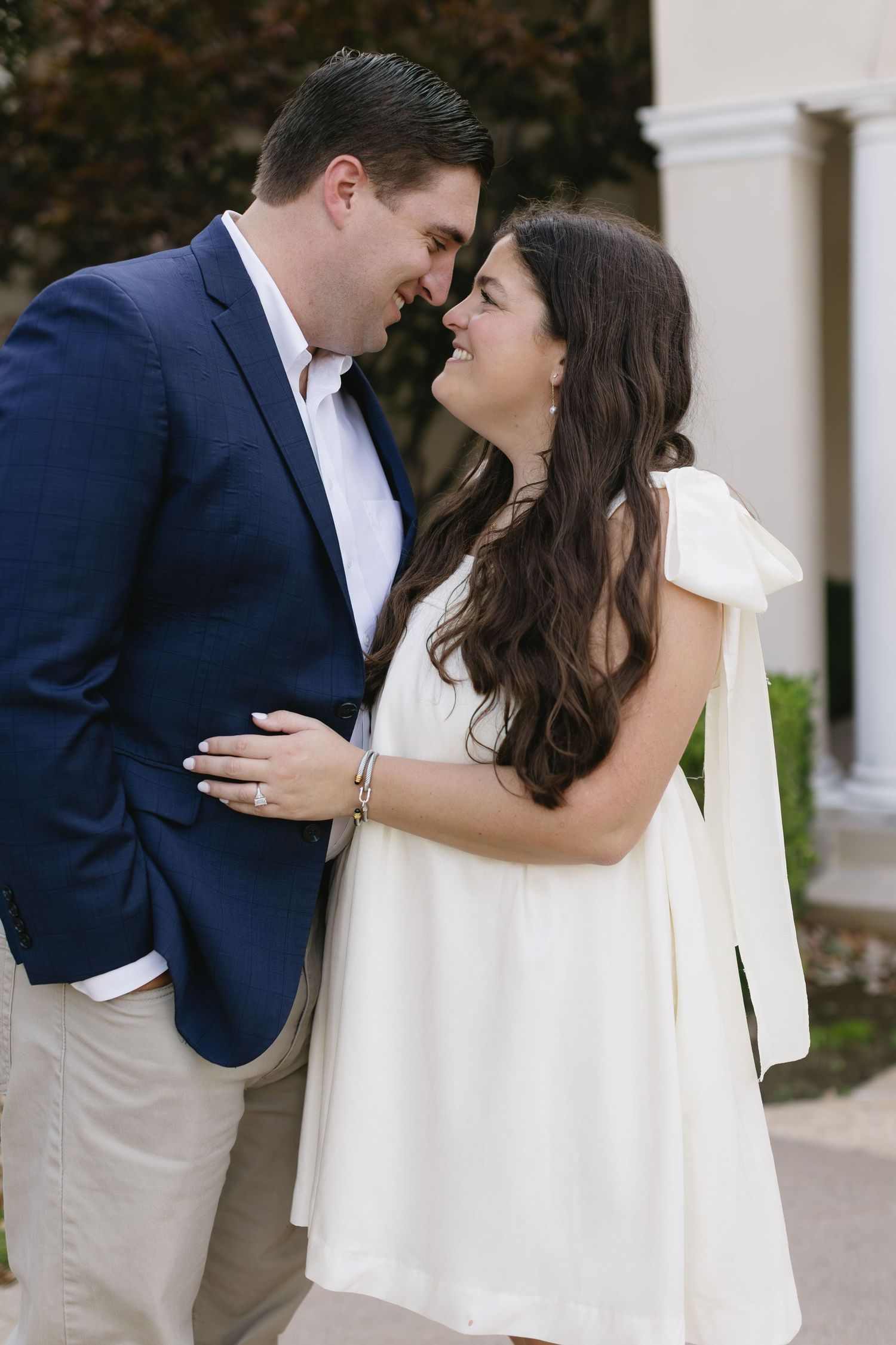 A couple in navy and white attire share romantic moments against a white columned backdrop.
