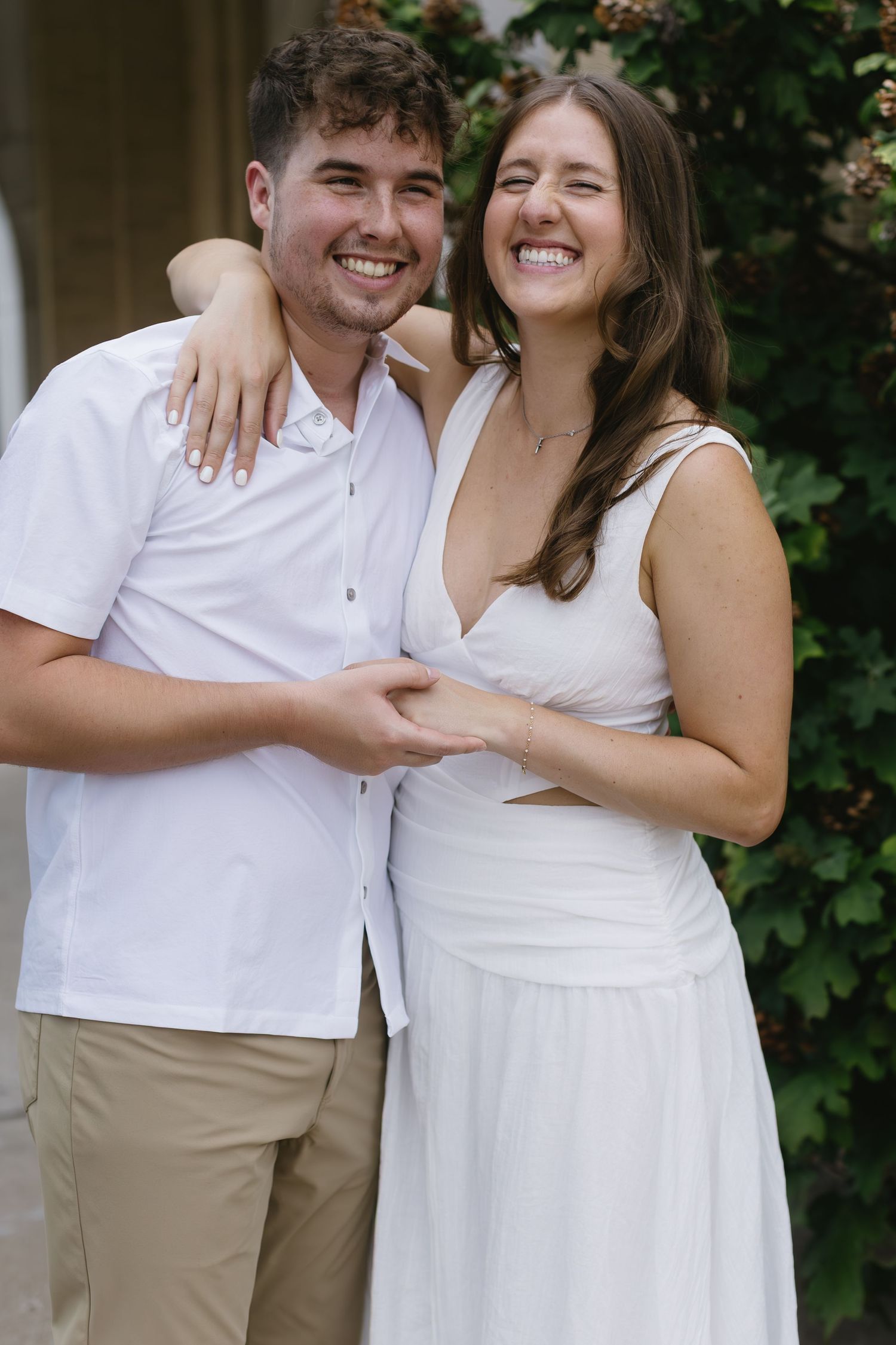 A joyful couple in white outfits embraces while laughing together during a photo session.