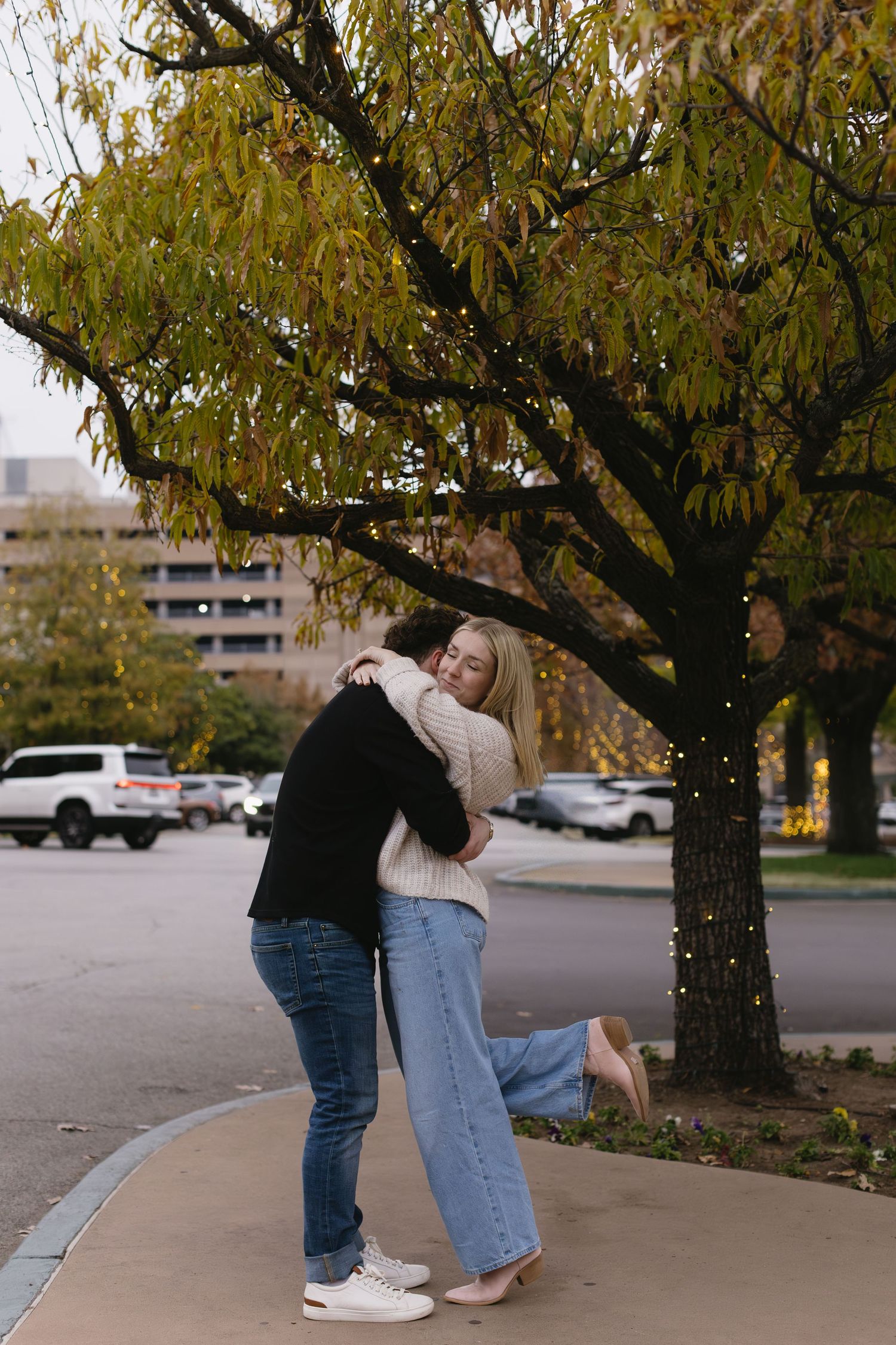 A couple shares romantic moments under yellow autumn trees in a parking lot.