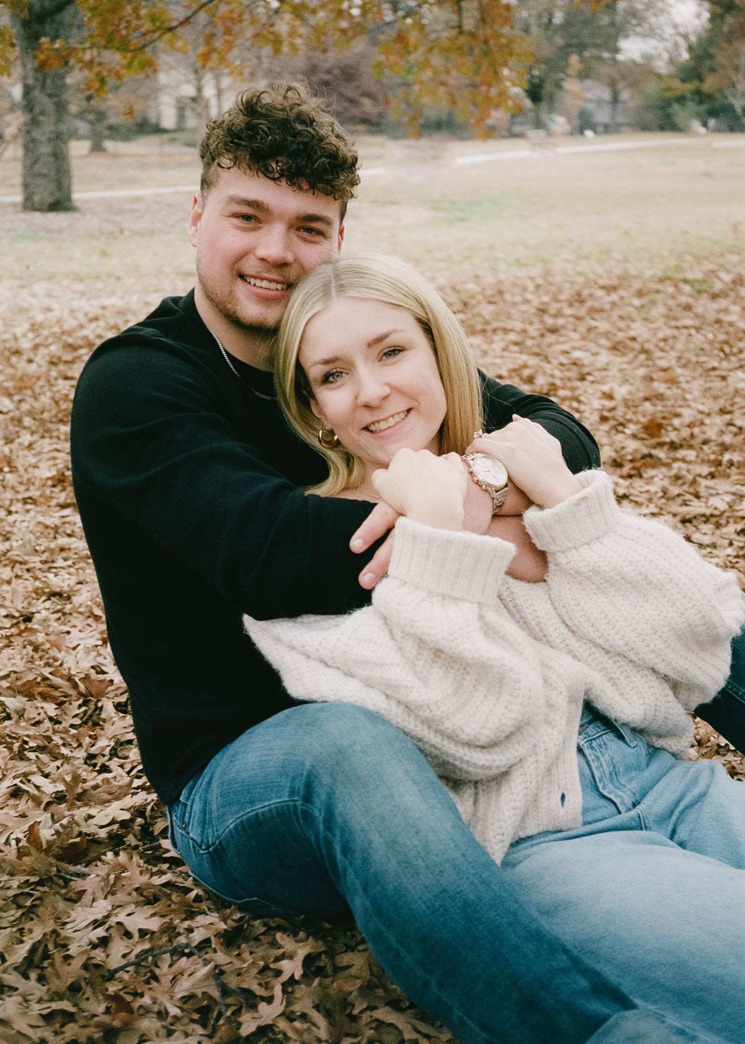A joyful autumn portrait of a couple sitting together on fallen leaves in casual wear.