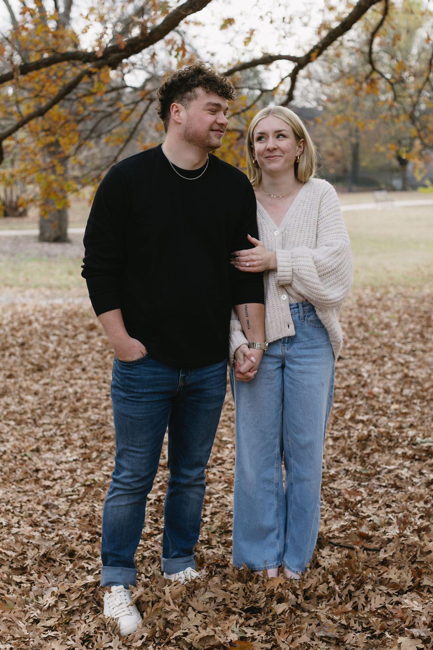 A couple poses together on fallen leaves during an autumn photoshoot.