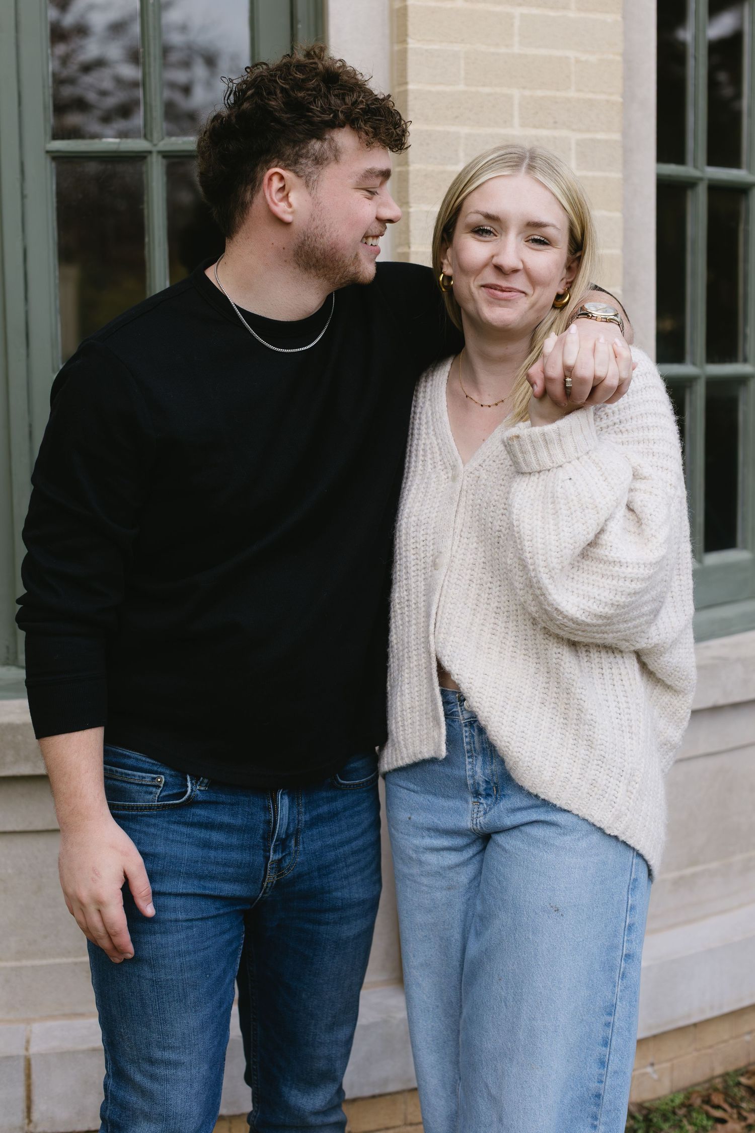 A sweet candid moment between a couple in matching casual wear standing by a window.