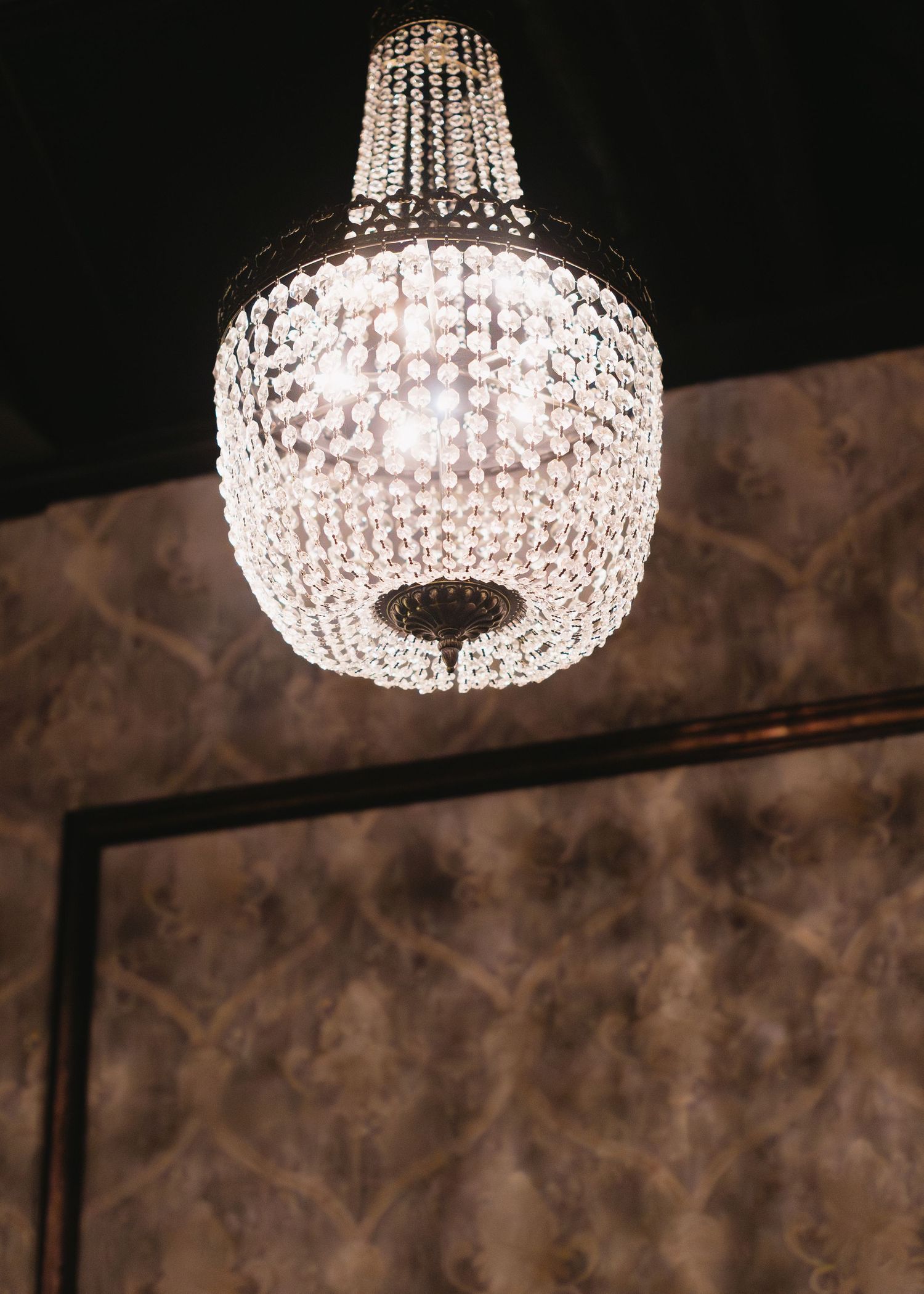 Crystal chandelier hanging from dark ceiling creates elegant ambiance in dimly lit space.