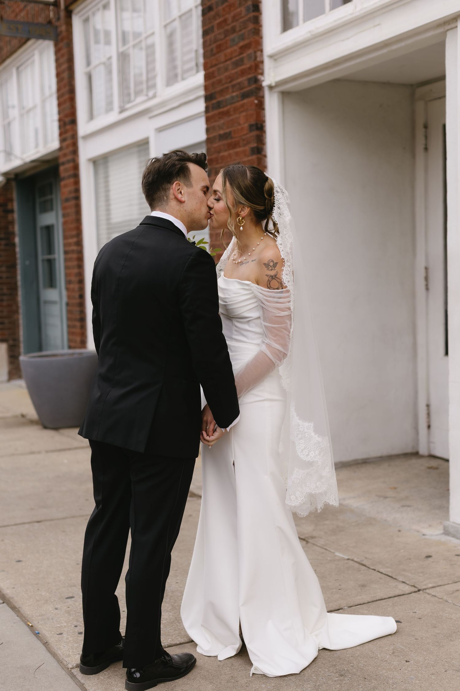 Intimate wedding couple moment captured against white columns and brick wall backdrop.