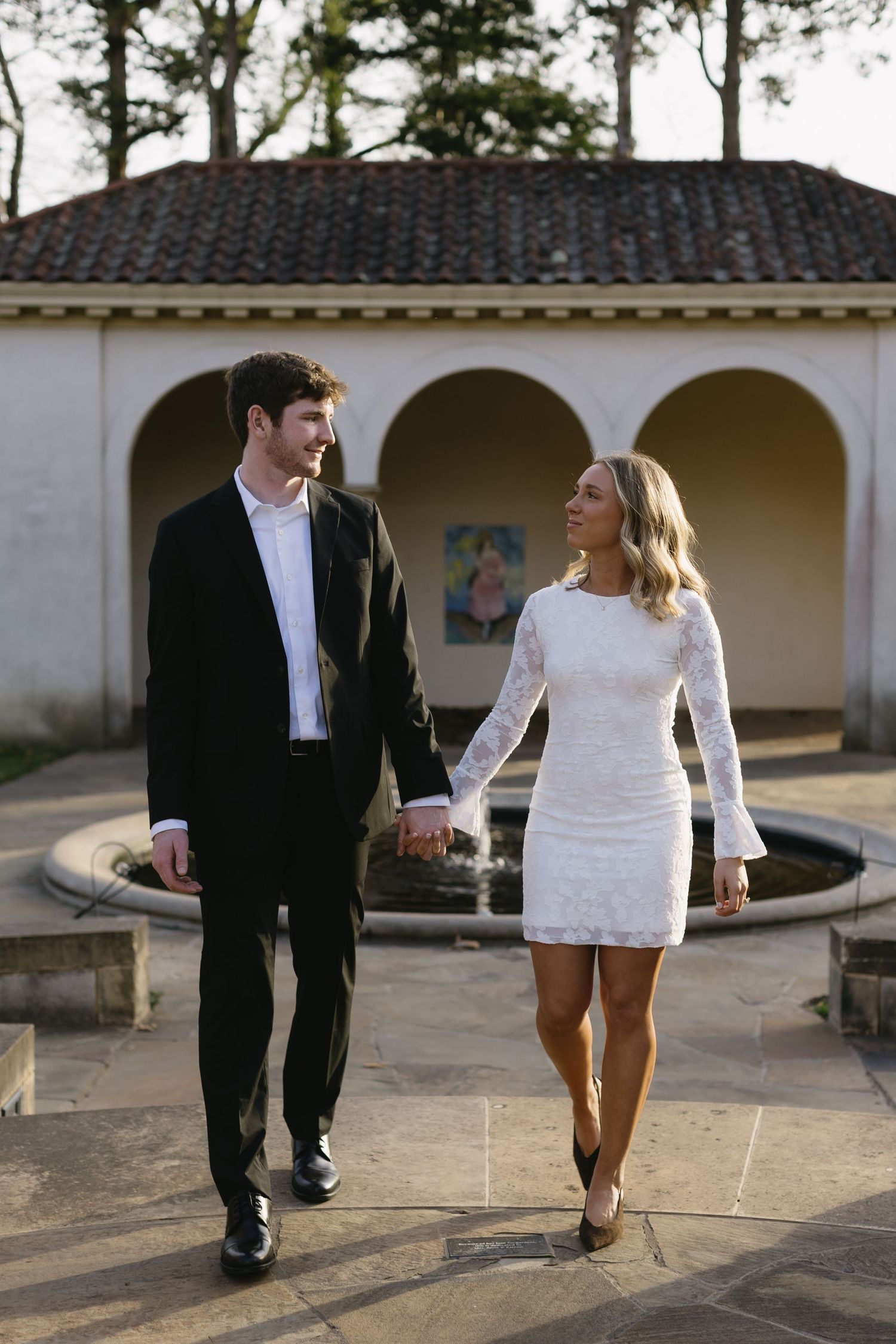 A couple strolls together along a Spanish-style courtyard with arched columns.