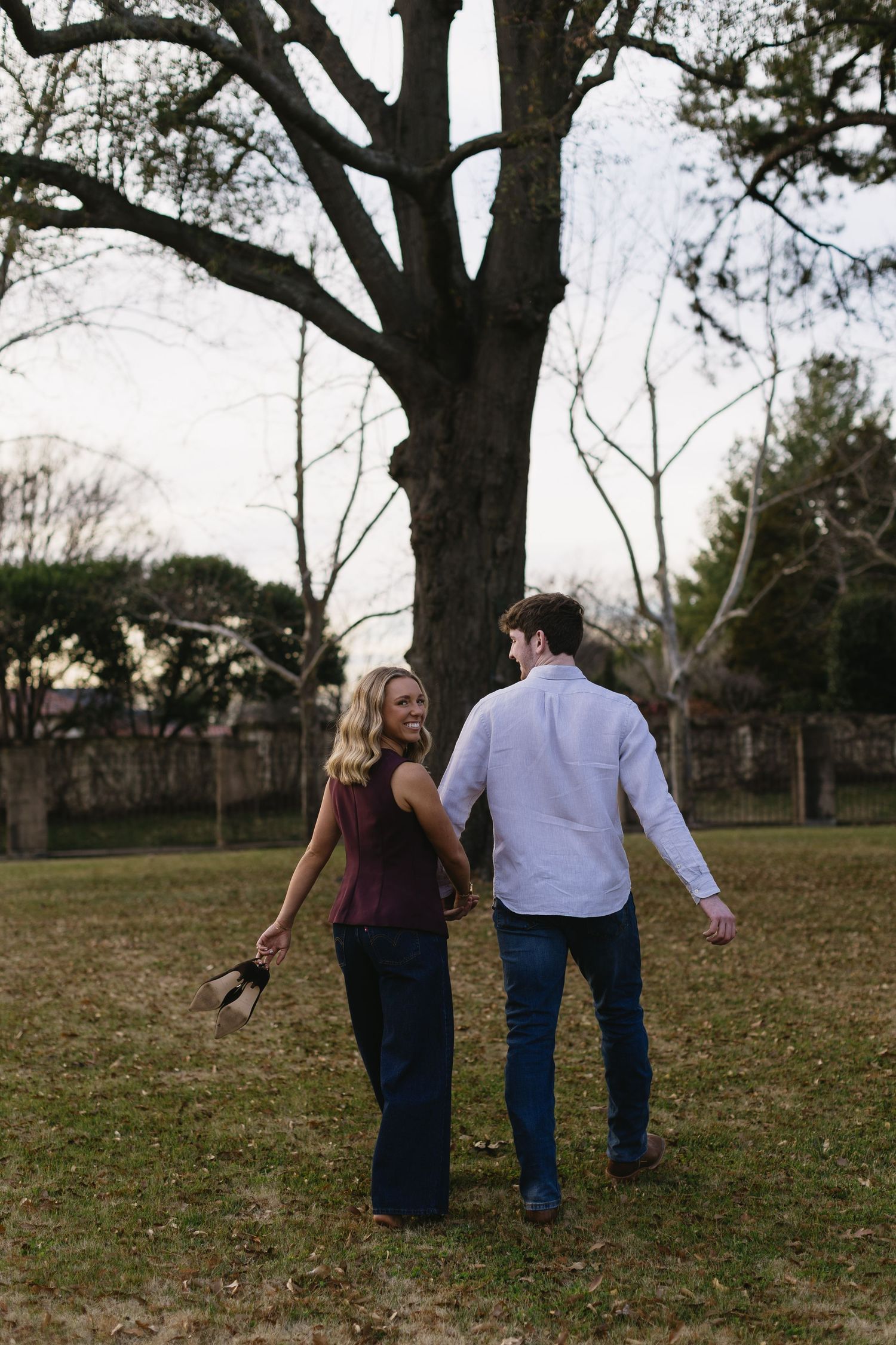 A couple strolling hand in hand across a grassy field with trees in the background.