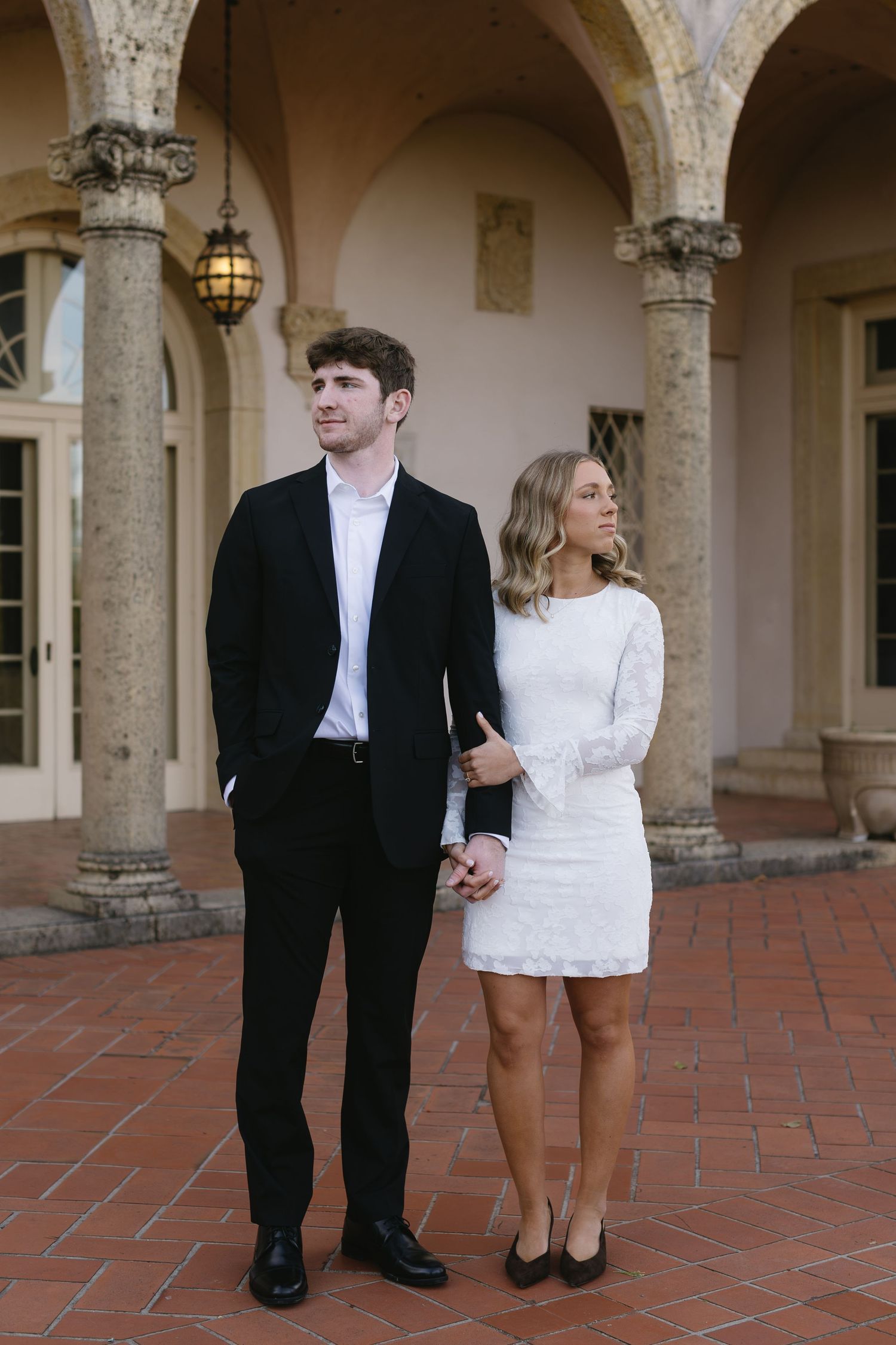 A couple in formal attire shares a romantic moment under an elegant archway with terracotta flooring.