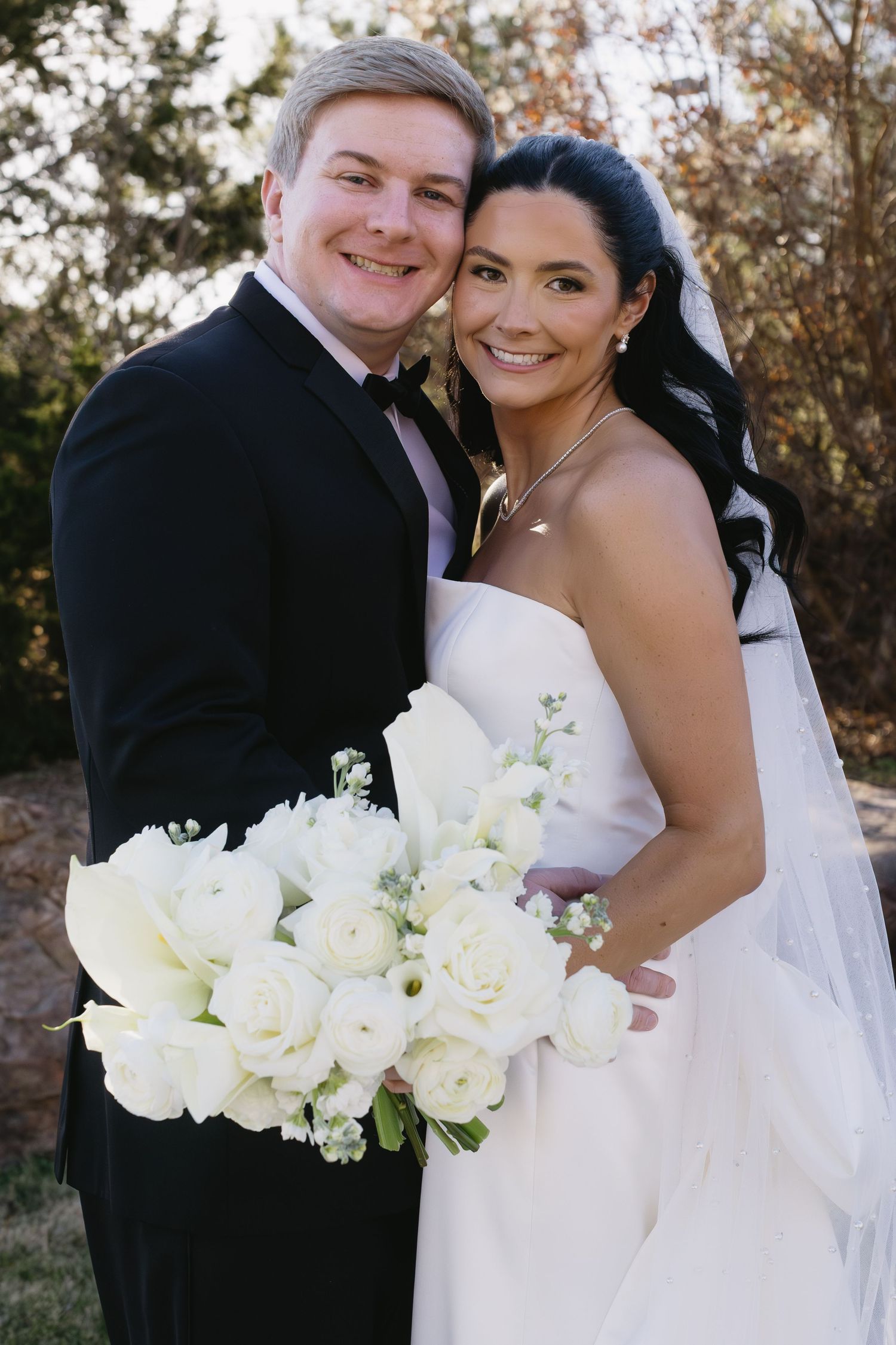 Wedding couple holding a bouquet of white roses outdoors in natural lighting.
