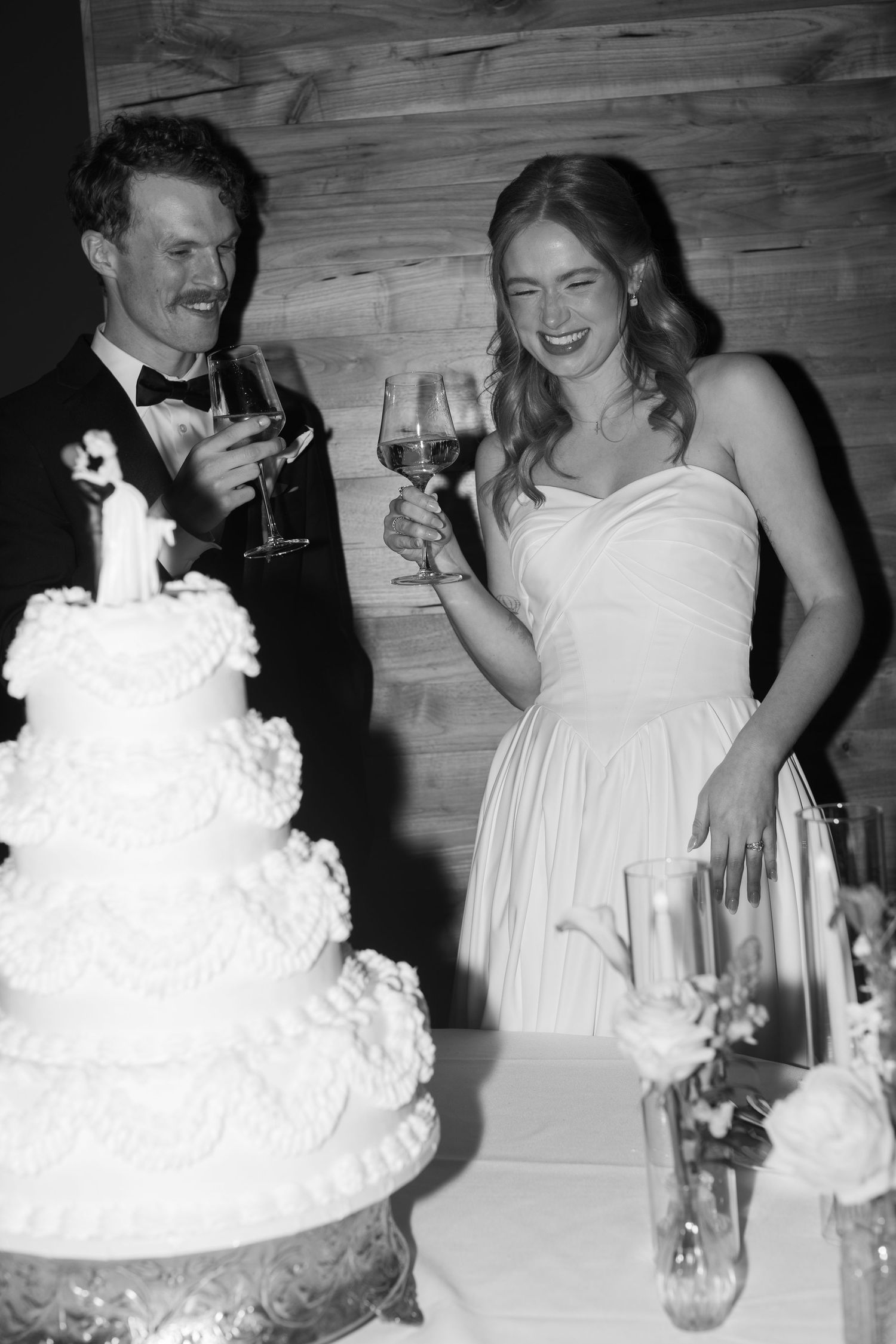 Newlyweds share laughter while cutting their white wedding cake at the reception.