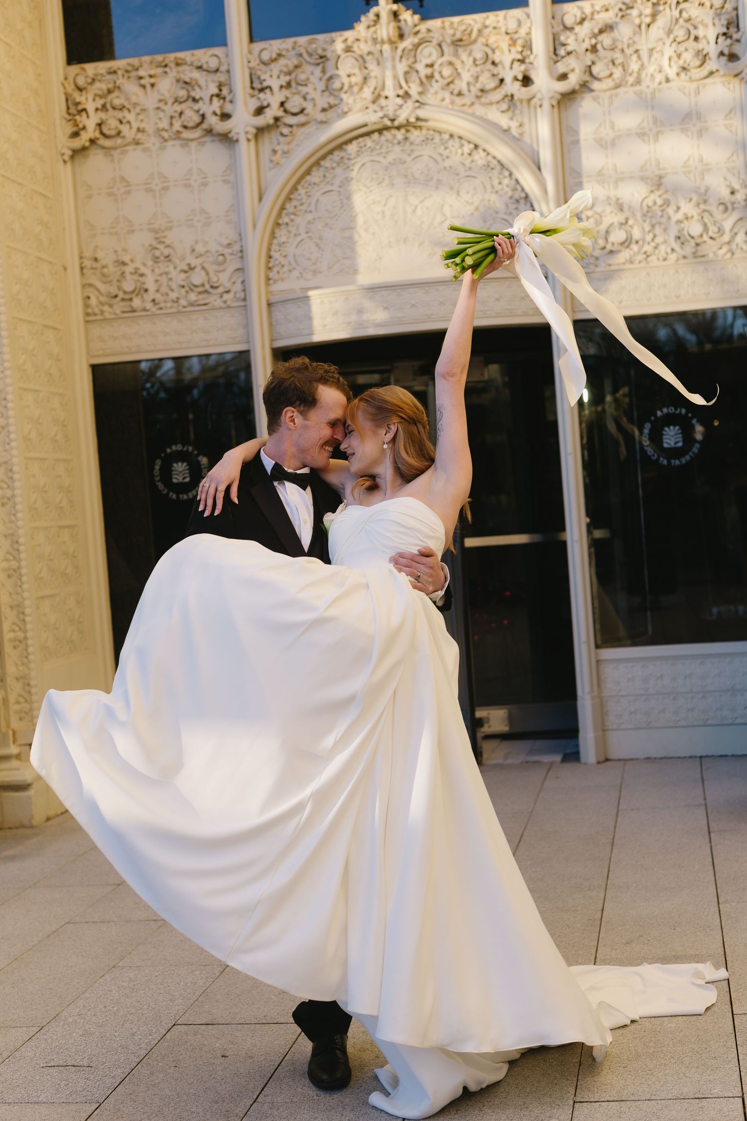 A bride and groom perform a dramatic dip dance move under an ornate stone archway.