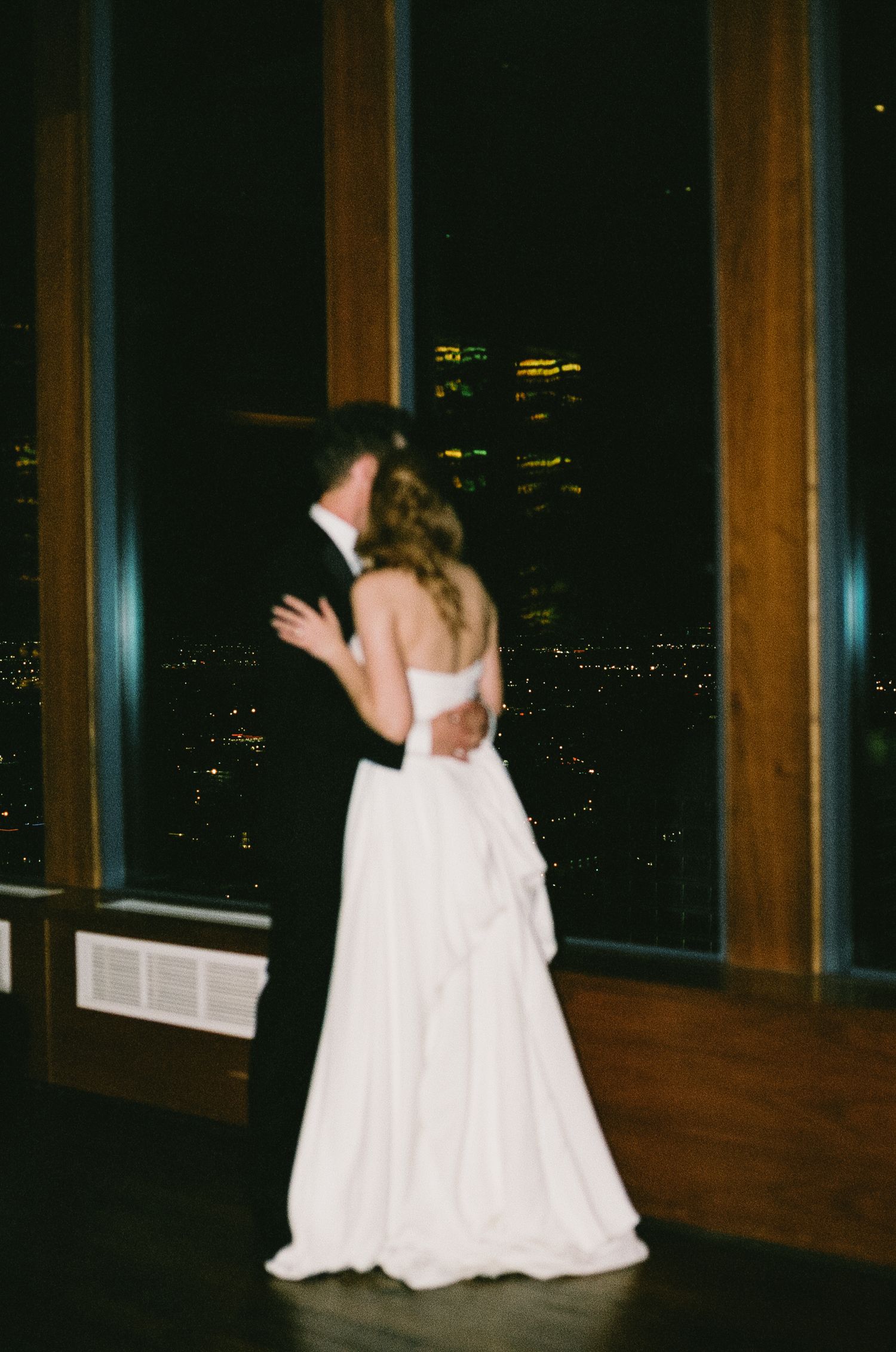 Couple dancing in an elegant venue with city lights visible through large windows.