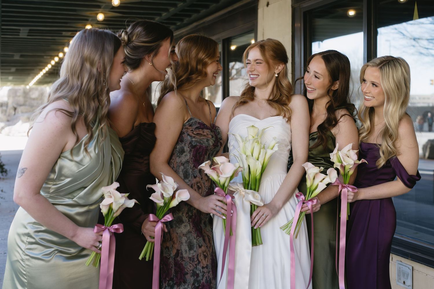 Wedding party in mixed purple and neutral dresses sharing candid moment outdoors.